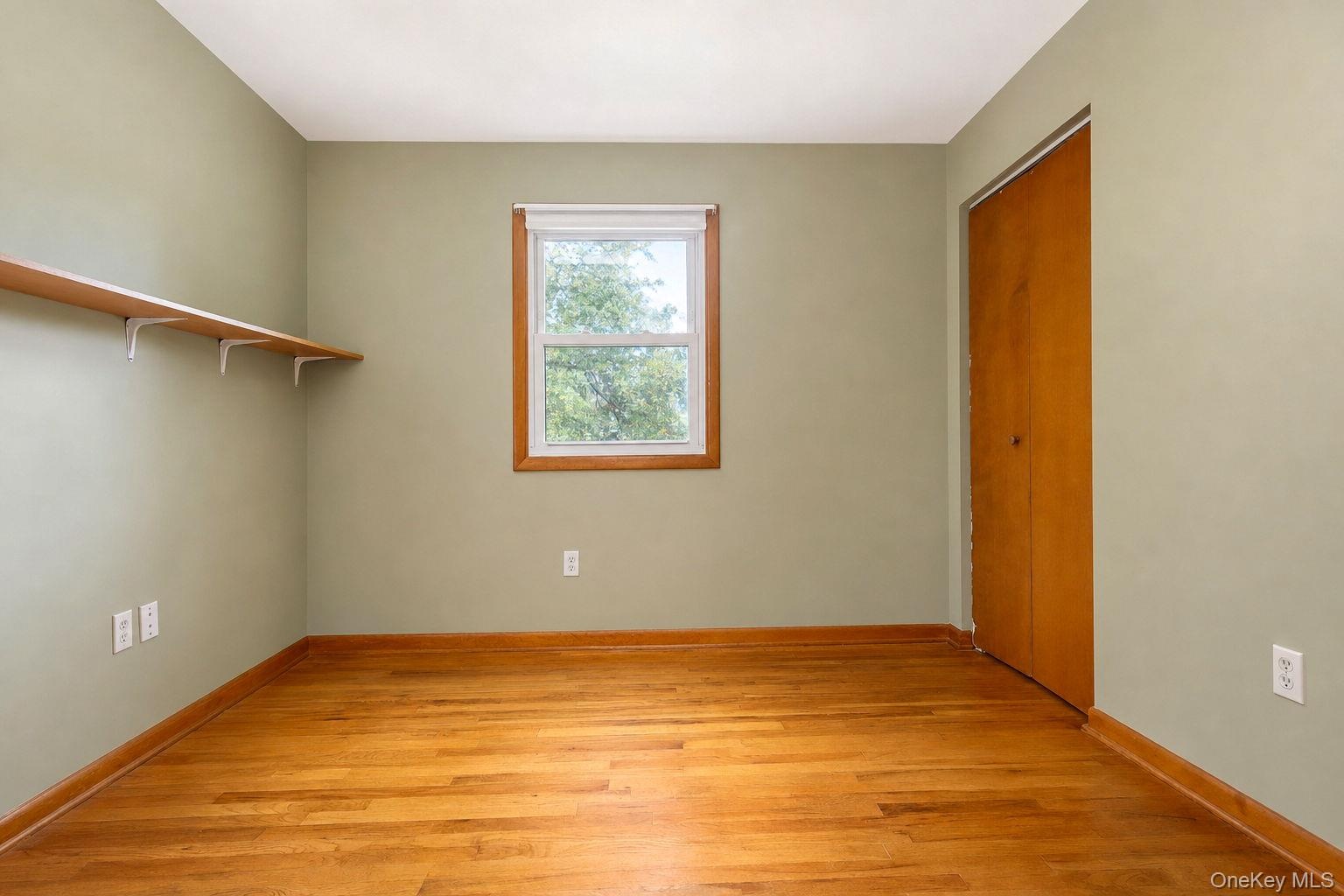Hardwood flooring, natural light via a single window with wood-trim casing, built-in wall shelving, and a wood-finish closet door