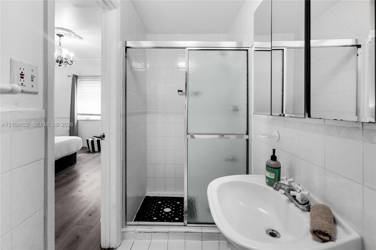 Shower enclosure with sliding glass doors, ceramic wall tiling, pedestal sink with chrome faucet, and triple-pane medicine cabinet