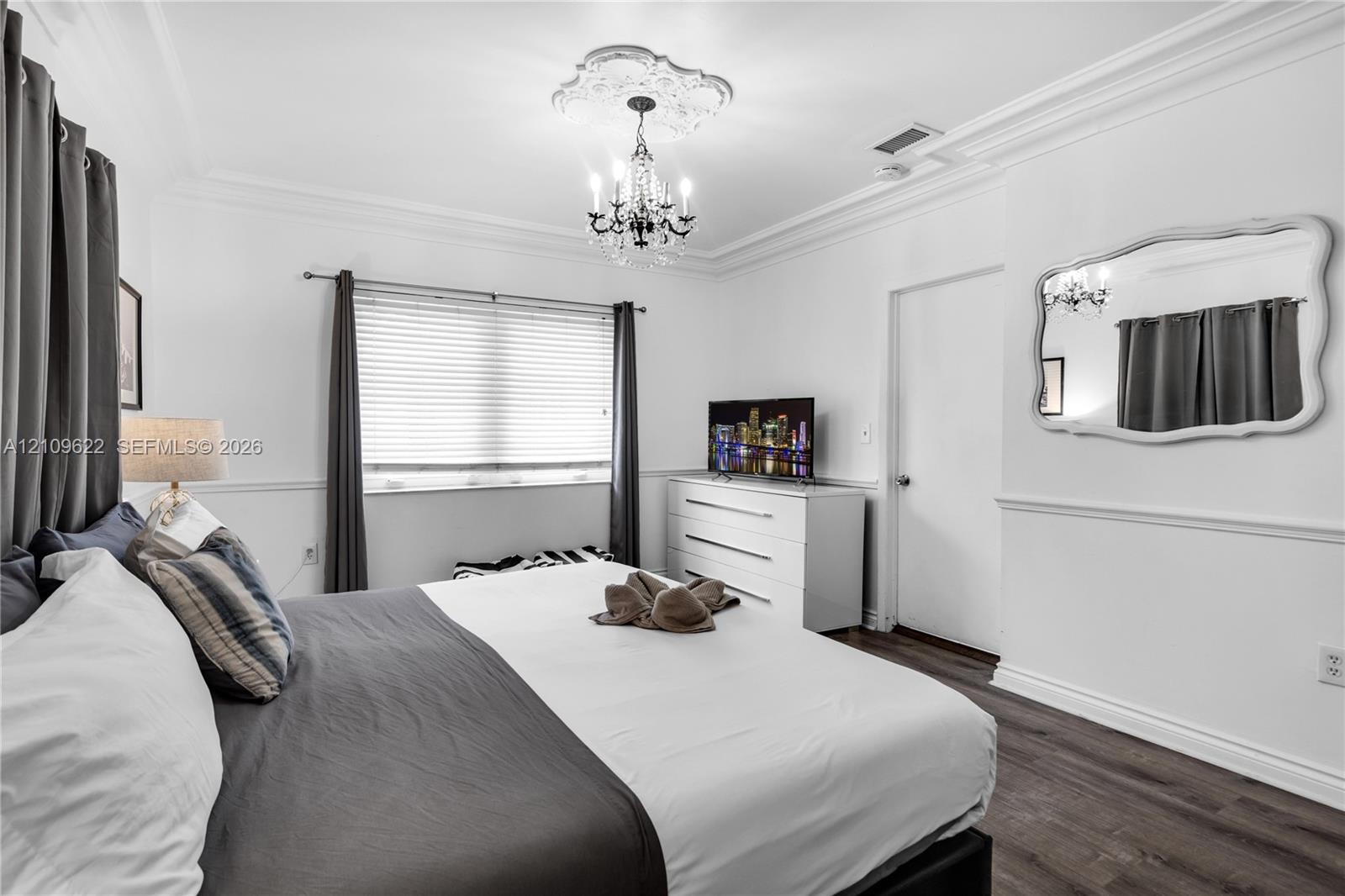 Room featuring crown molding, chair rail trim, wood-finish flooring, a decorative ceiling medallion, and a multi-arm chandelier