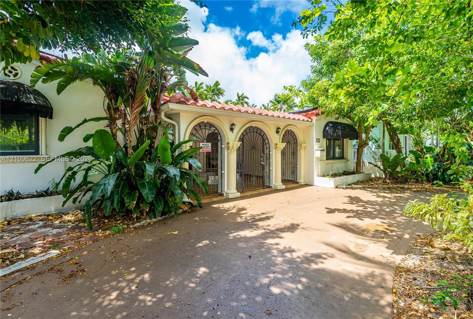 Spanish-style exterior featuring a covered entryway with arched openings, decorative columns, red clay tile roofing, and metal security gates