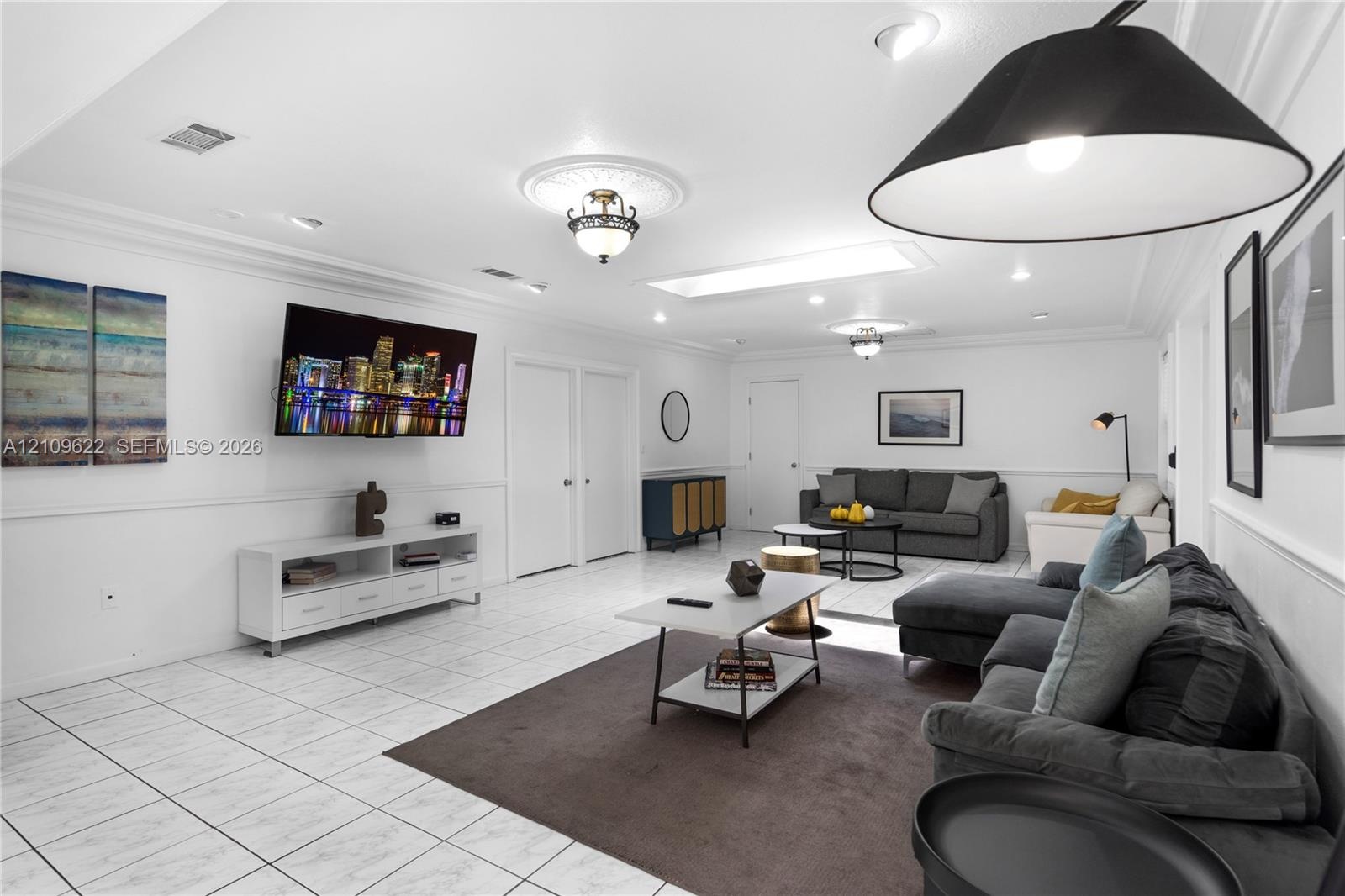 Spacious room featuring tile flooring, crown molding, chair rail trim, recessed lighting, and a skylight