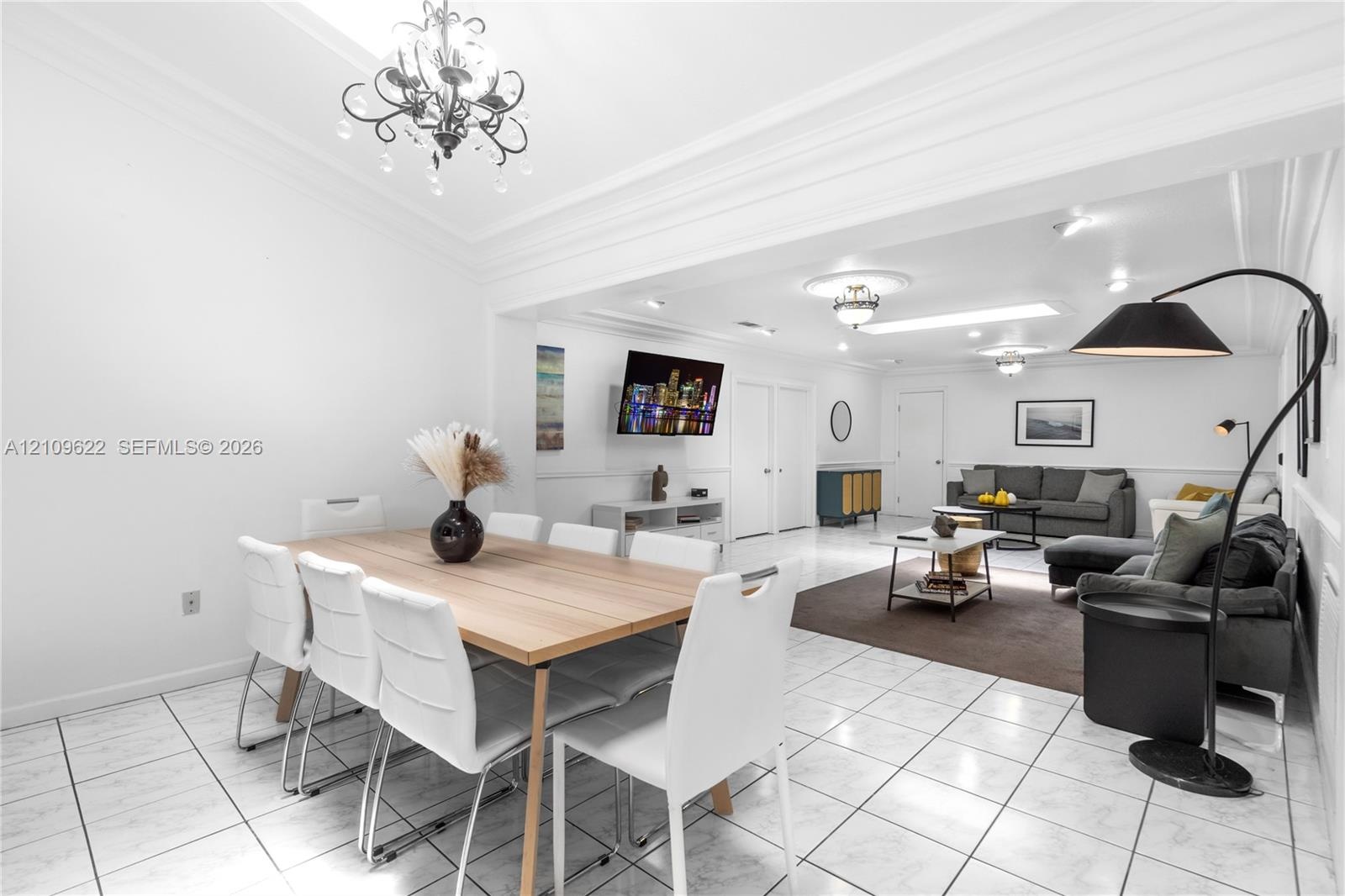 Open-concept living and dining area featuring large-format tile flooring, crown molding, chair rail detailing, recessed lighting, and a decorative cry