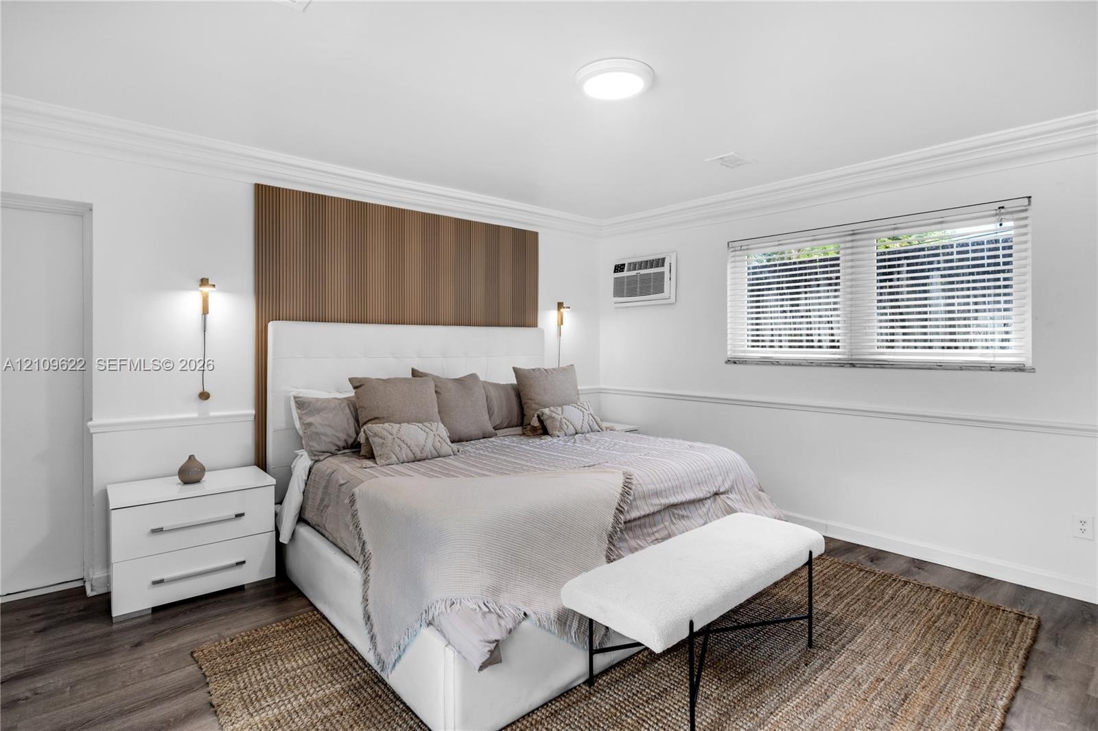 Bedroom featuring crown molding, chair rail trim, wood-finish flooring, a vertical wood-panel accent wall, and wall-mounted gold-toned light fixtures