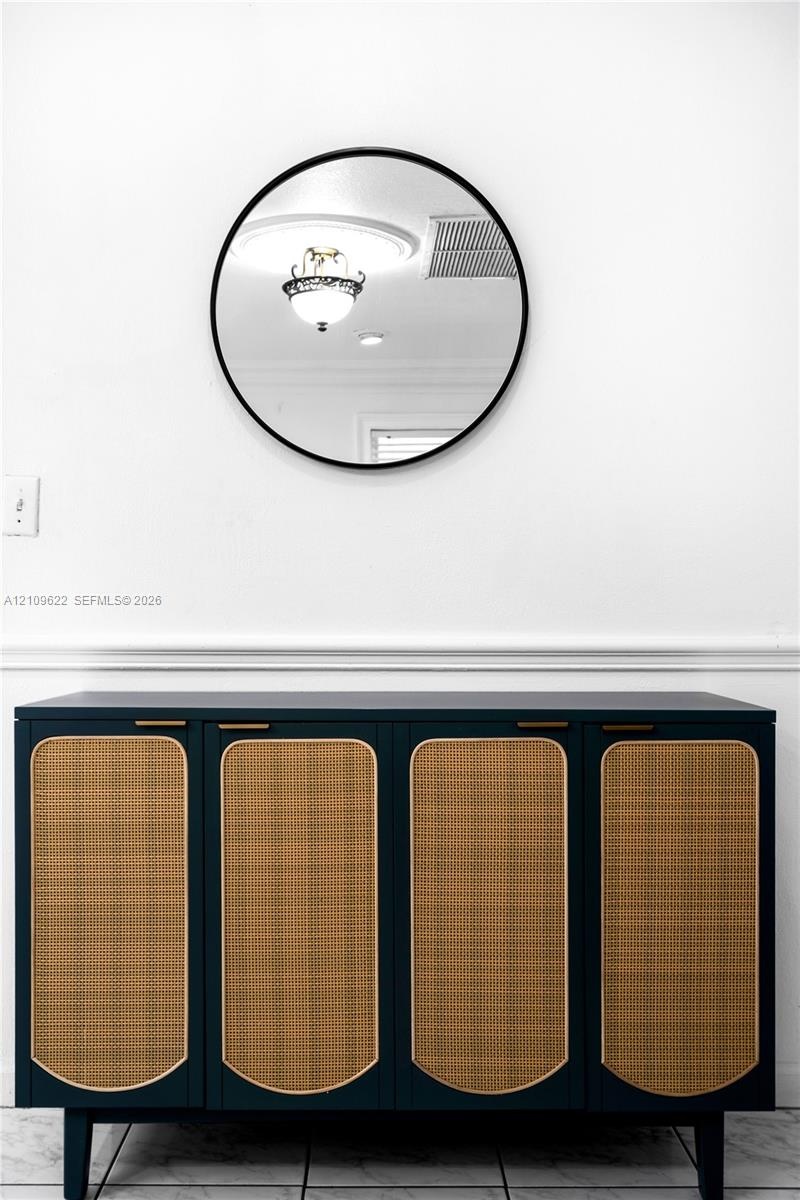 Circular wall mirror with a matte black frame, set above a built-in dark cabinetry unit featuring woven rattan door panels and brass-finish hardware