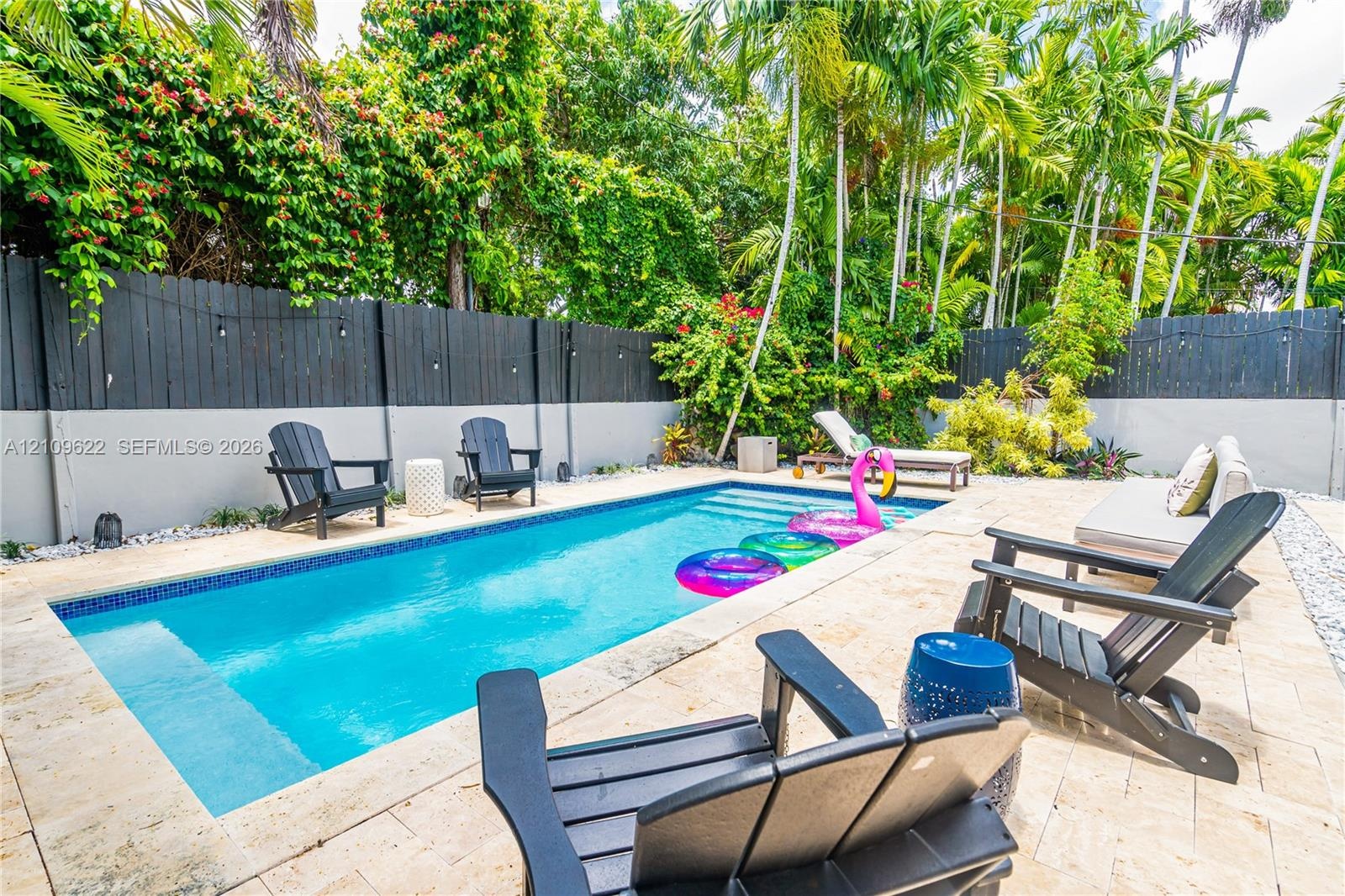Rectangular in-ground pool with stone-tiled decking, enclosed by a two-tone privacy fence and mature perimeter landscaping