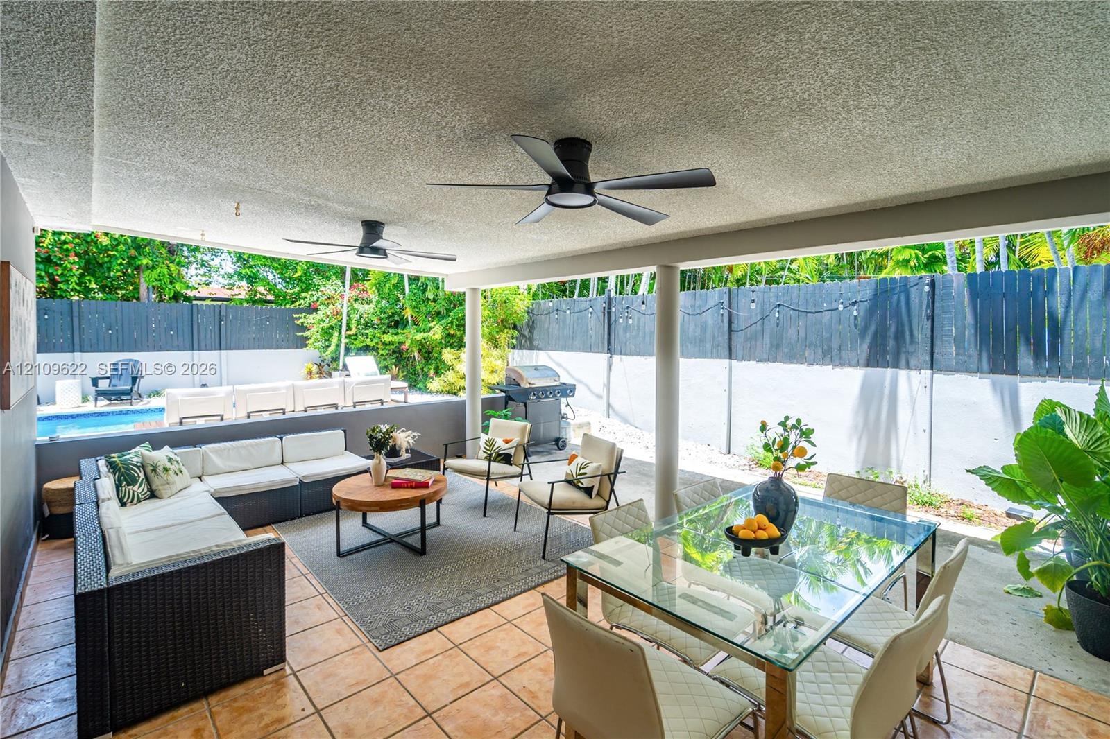 Covered patio featuring tiled flooring, two matte black ceiling fans, and a solid perimeter privacy fence