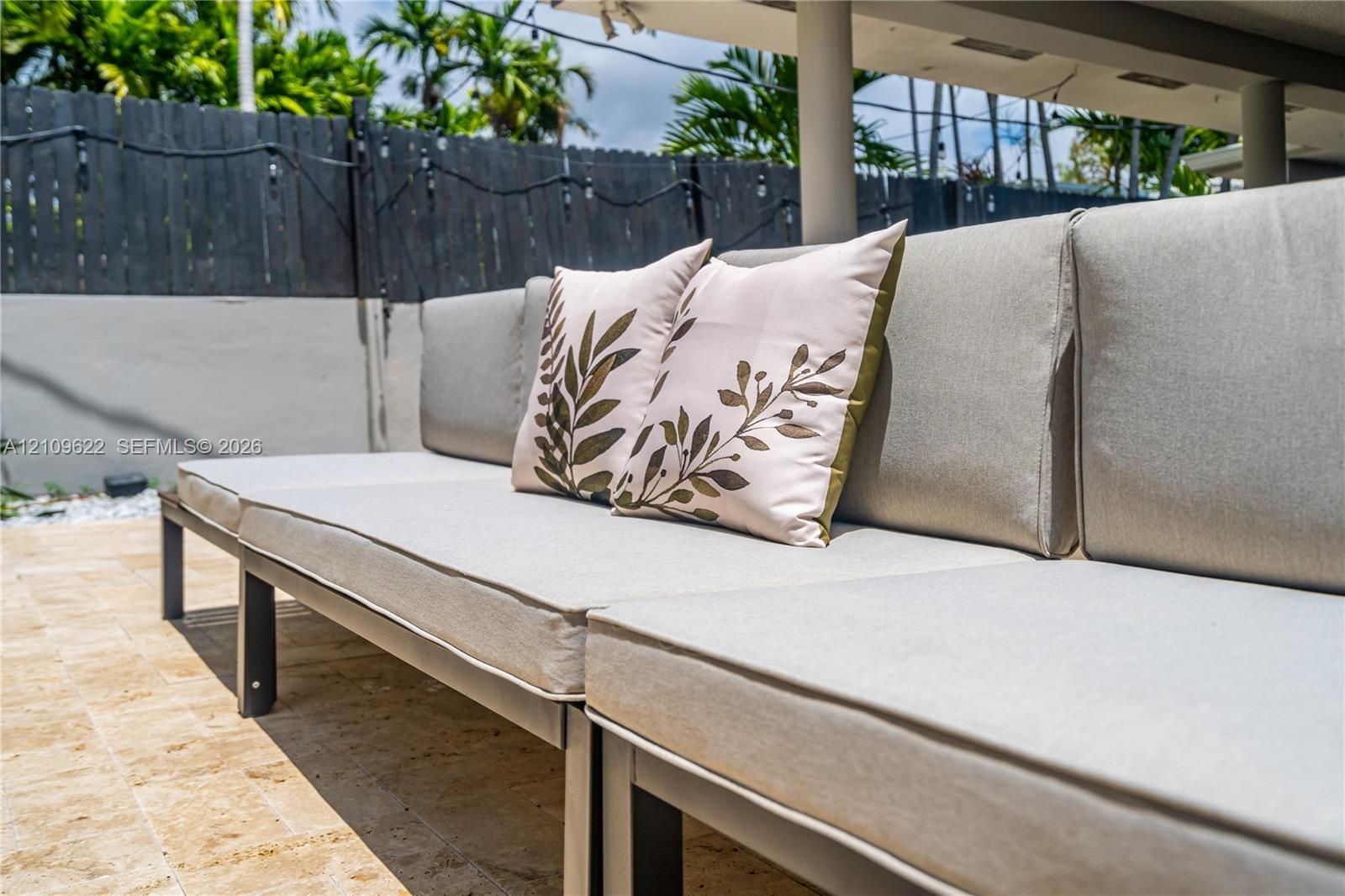 Outdoor patio featuring natural stone pavers, a covered lanai with structural columns, and a perimeter privacy fence