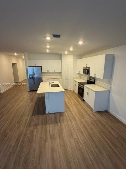 Kitchen featuring white cabinetry, solid-surface countertops, center island with an integrated stainless-steel sink, stainless-steel appliances, and w