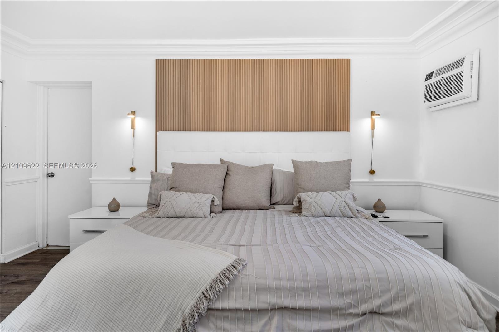 Wood-slat accent paneling, white upholstered headboard, wall-mounted metallic light fixtures, chair rail molding, and wood-finish flooring