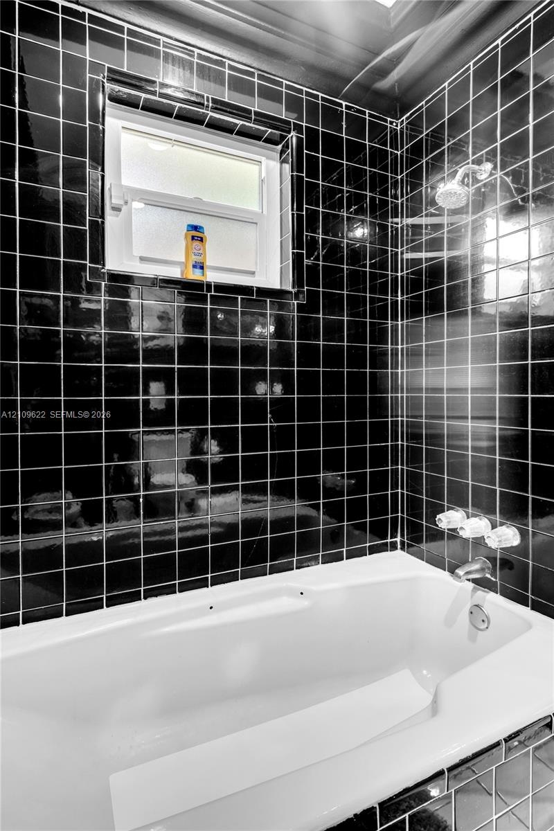Full-height black square tile surround, white soaking tub, chrome multi-handle faucet assembly, adjustable chrome shower head, and an operable window