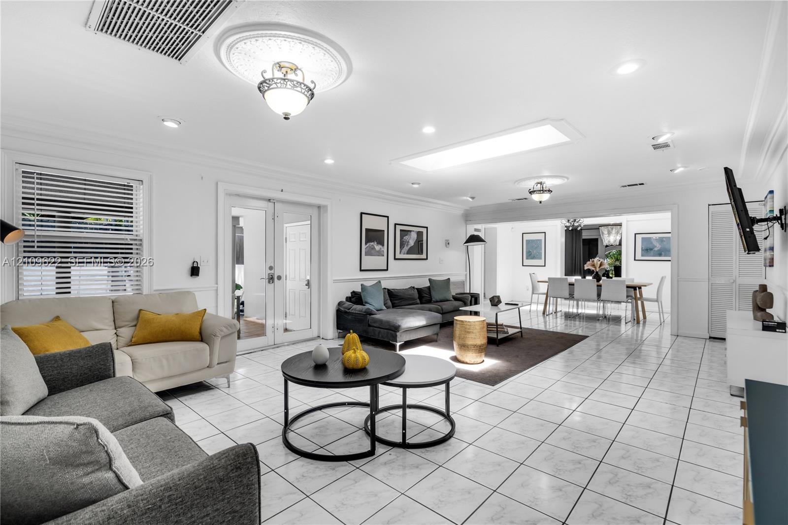 Open-concept living space featuring large-format tile flooring, multiple recessed light fixtures, a prominent skylight, ceiling-mounted decorative lig