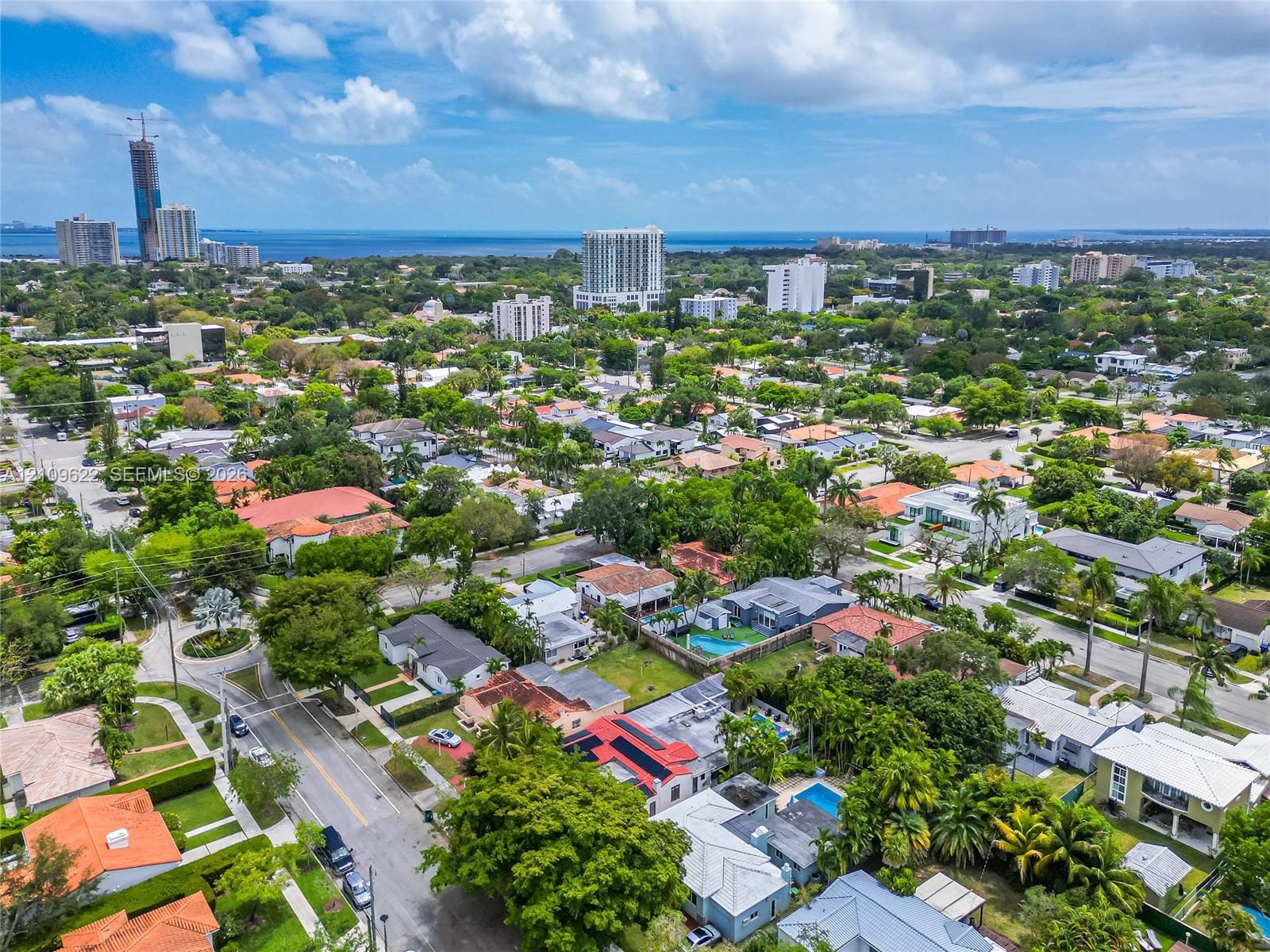 Aerial perspective of a coastal residential area featuring mature tree canopy, varied architectural styles, paved street infrastructure, and proximity