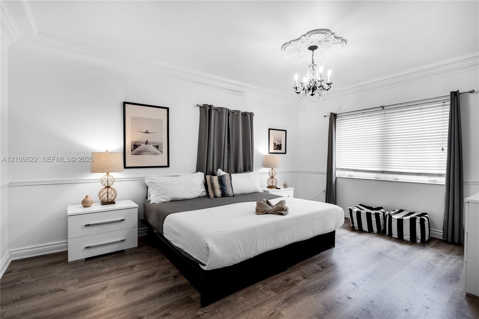 Bedroom featuring wood-finish flooring, crown molding, decorative chair rail, an ornate ceiling medallion, and a multi-arm crystal chandelier