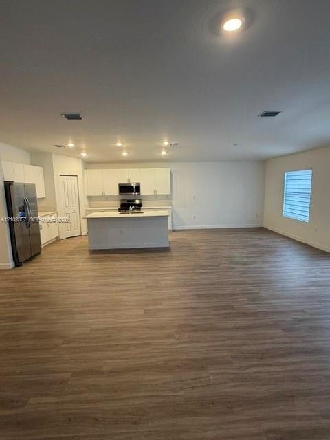 Open-concept kitchen featuring white shaker cabinetry, a center island with a solid surface countertop, wood-finish flooring, and stainless steel appl