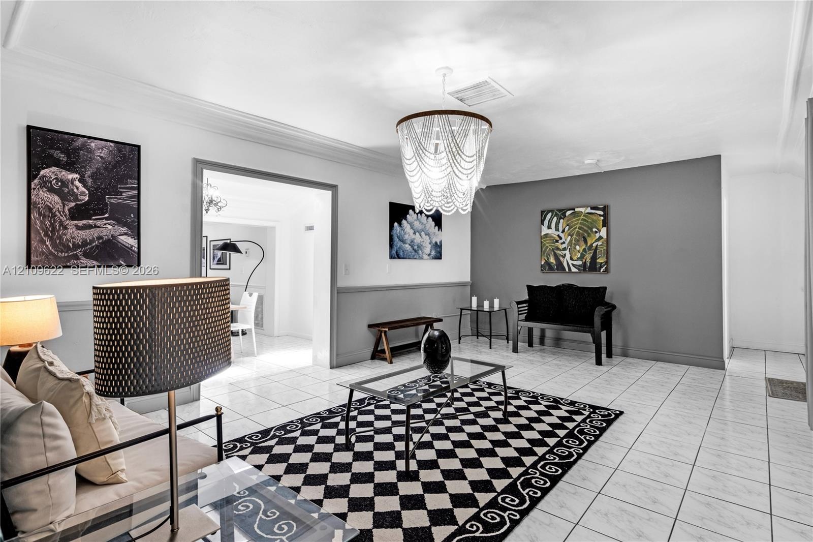 Living space featuring large-format tile flooring, two-tone wall paint, waist-high chair rail molding, and a tiered chandelier fixture