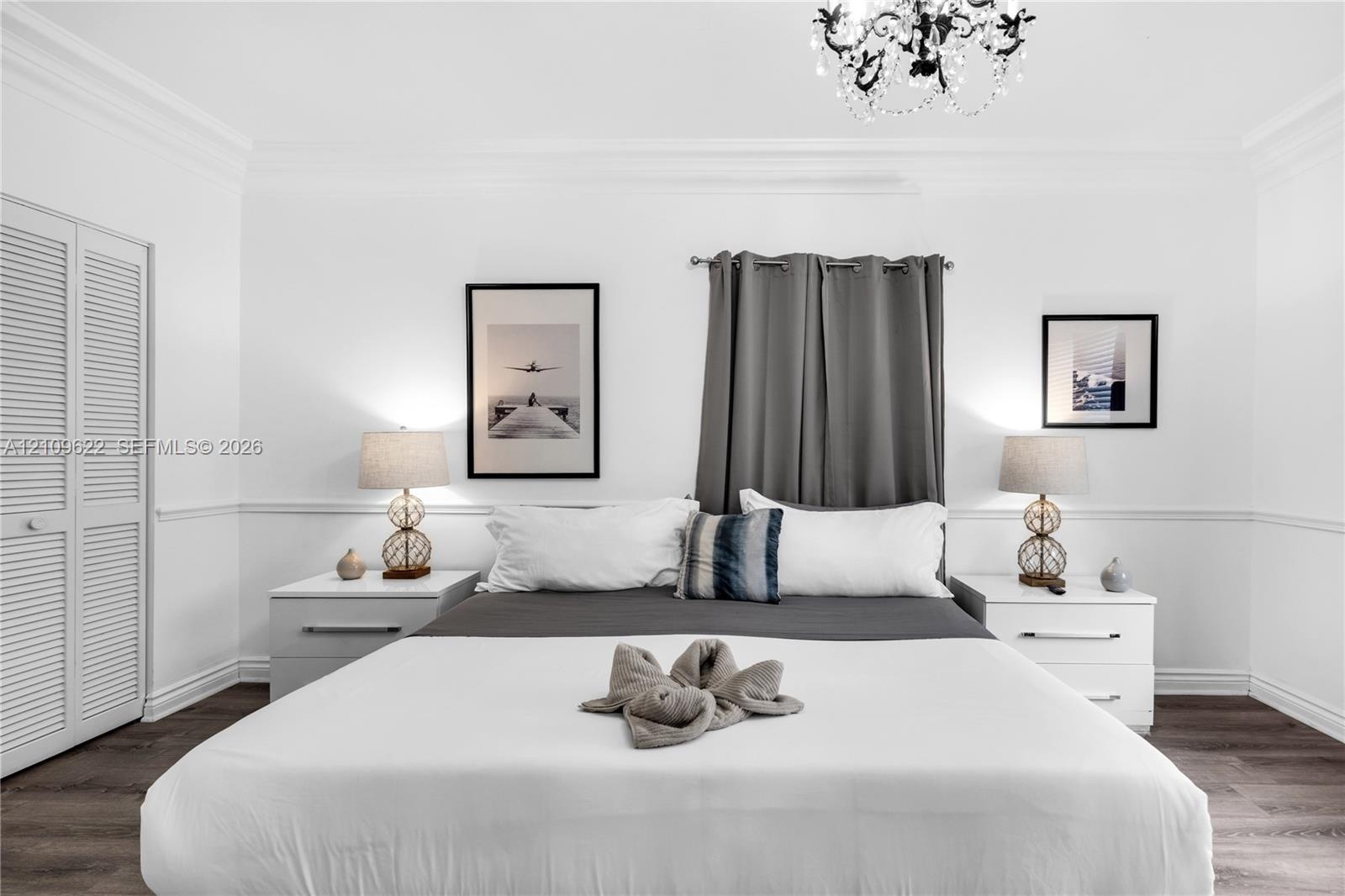 Bedroom featuring wood-finish flooring, crown molding, chair rail trim, louvered closet doors, and an ornate crystal chandelier