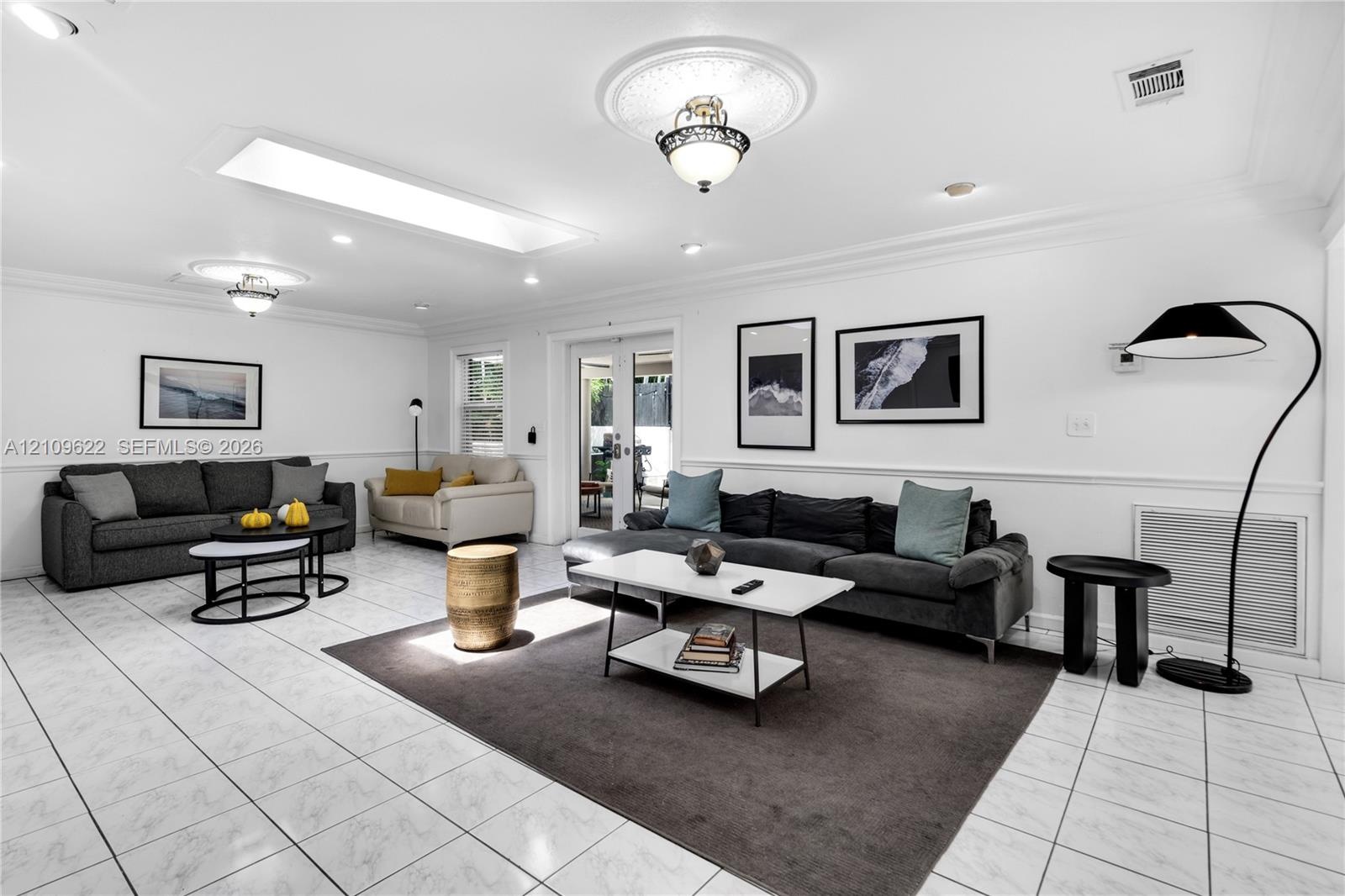 Spacious living area featuring polished tile flooring, decorative ceiling medallions, recessed lighting, a rectangular skylight, and glass-paneled pat