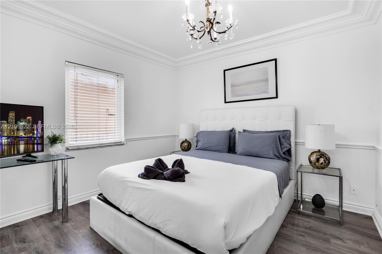 Wood-finish flooring, crown molding, wainscoting, and an ornate multi-arm chandelier