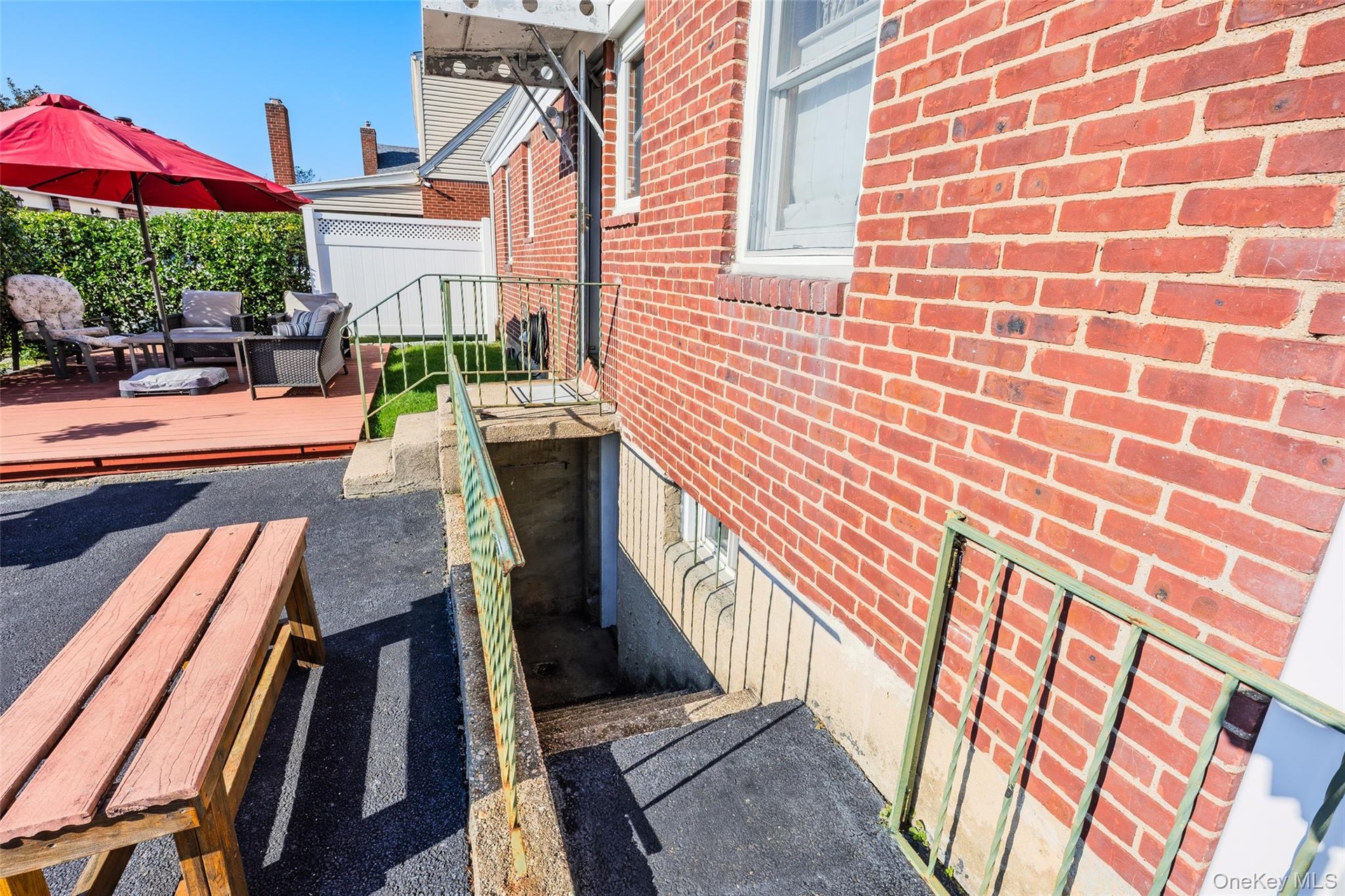 Red brick exterior featuring a wood deck, paved ground surface, and metal stair railing