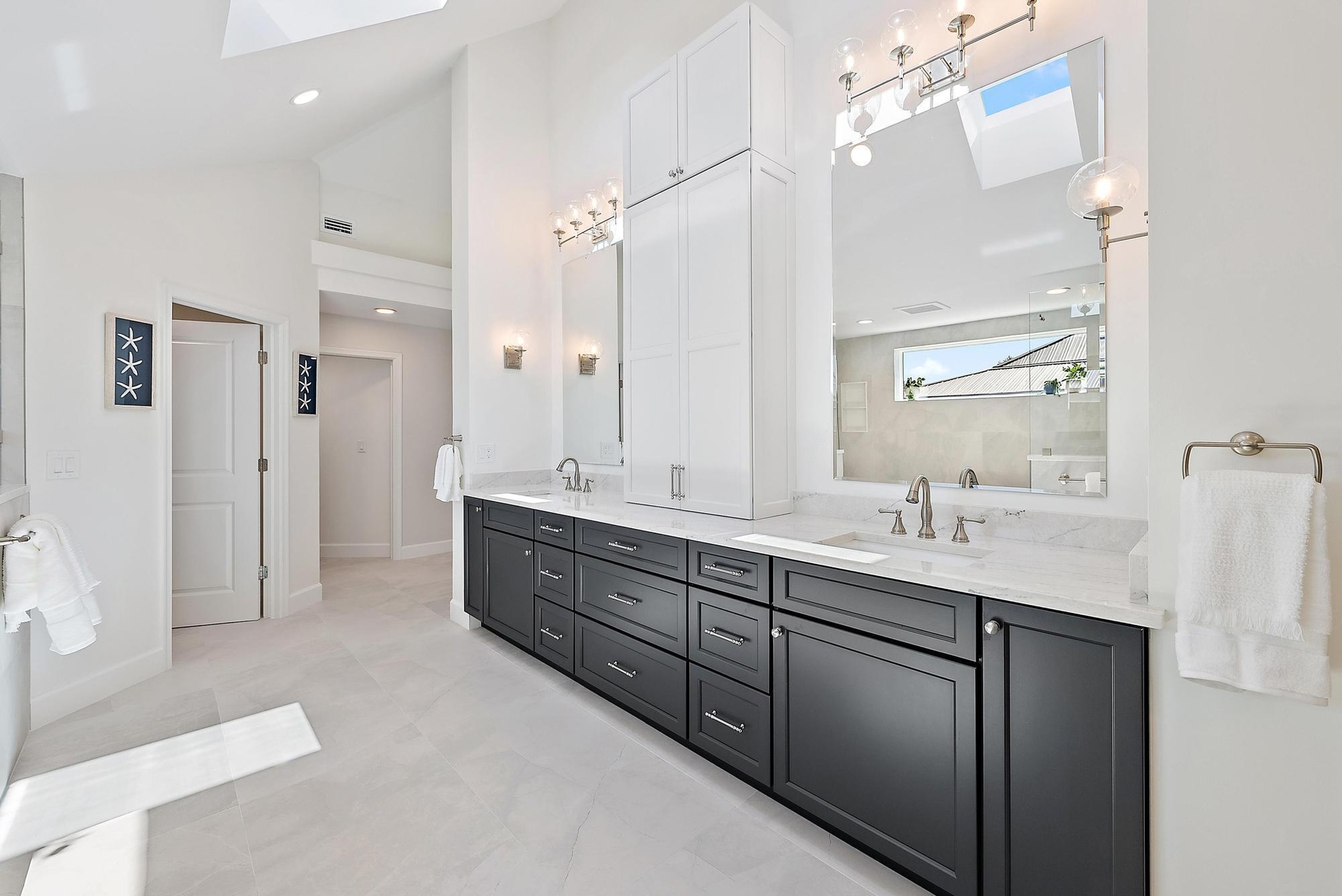 Dual-vanity bathroom featuring dark cabinetry, expansive stone countertops, integrated floor-to-ceiling storage, skylights, and polished metal fixture