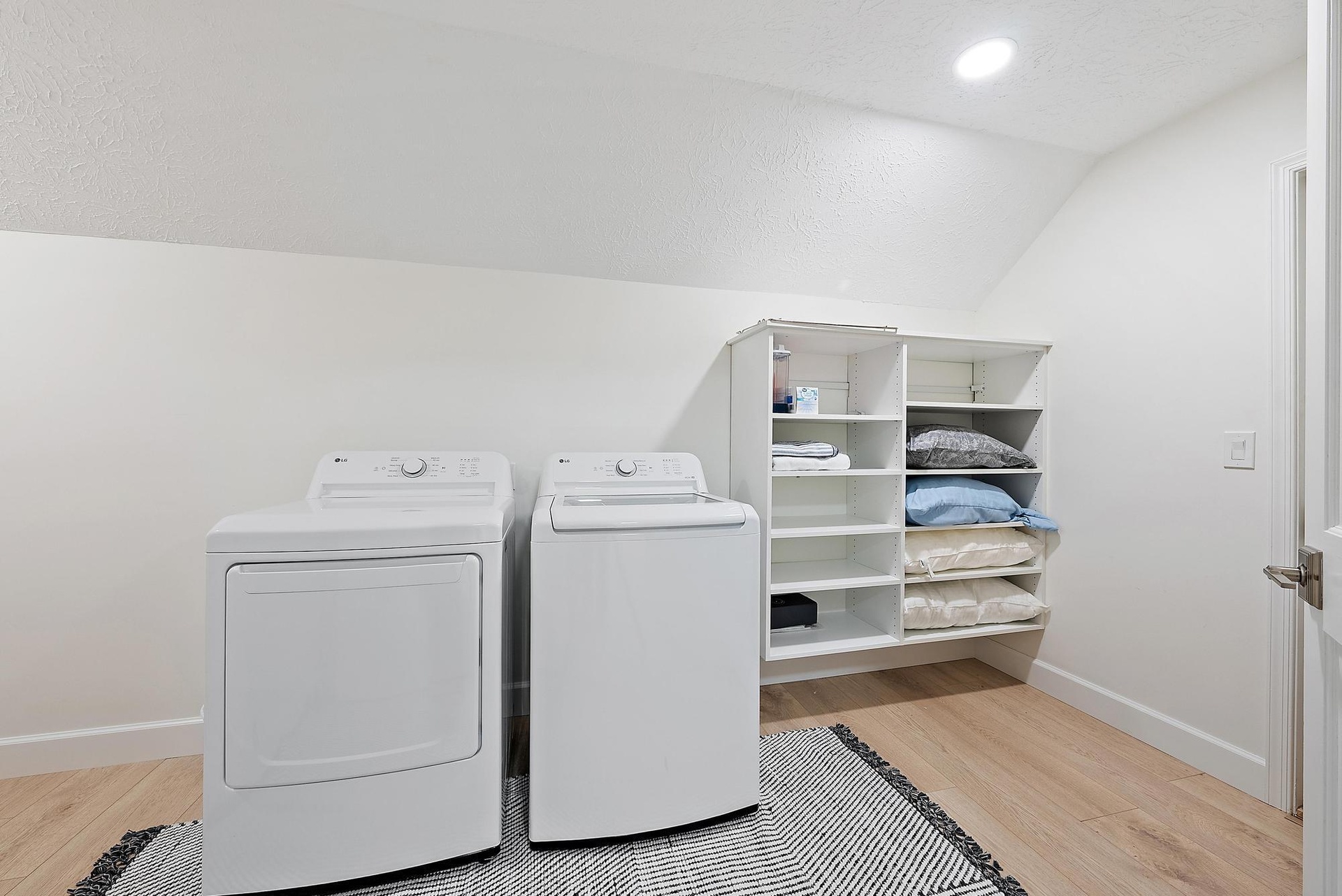 Dedicated laundry space featuring wood-finish flooring, recessed lighting, and wall-mounted white built-in shelving