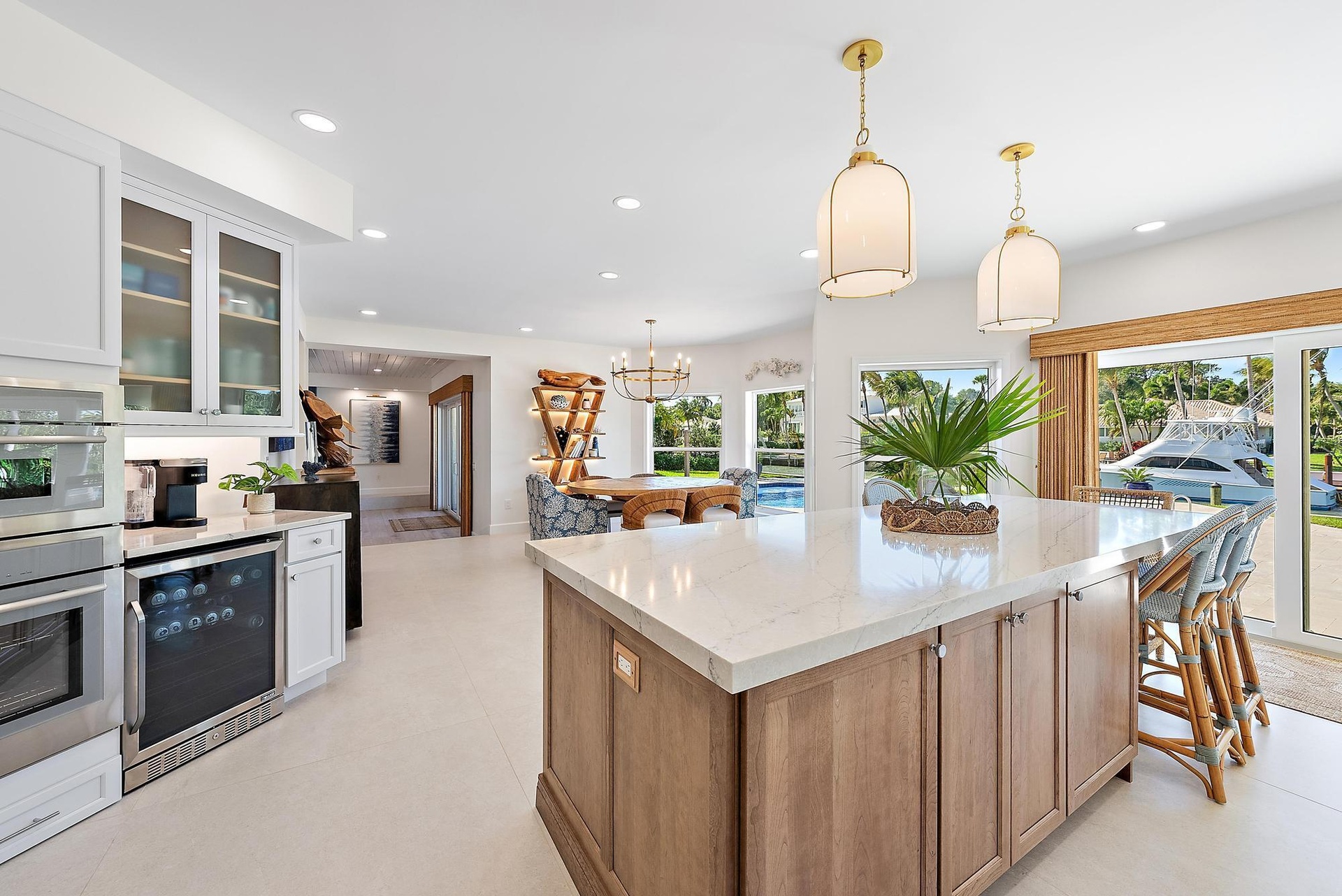 Kitchen featuring a large central island with light-toned stone surfacing, white cabinetry, built-in dual oven, under-counter wine refrigerator, and h