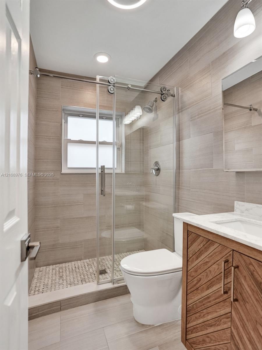 Bathroom featuring a walk-in shower with sliding glass door, linear tile surround, and pebble-style floor