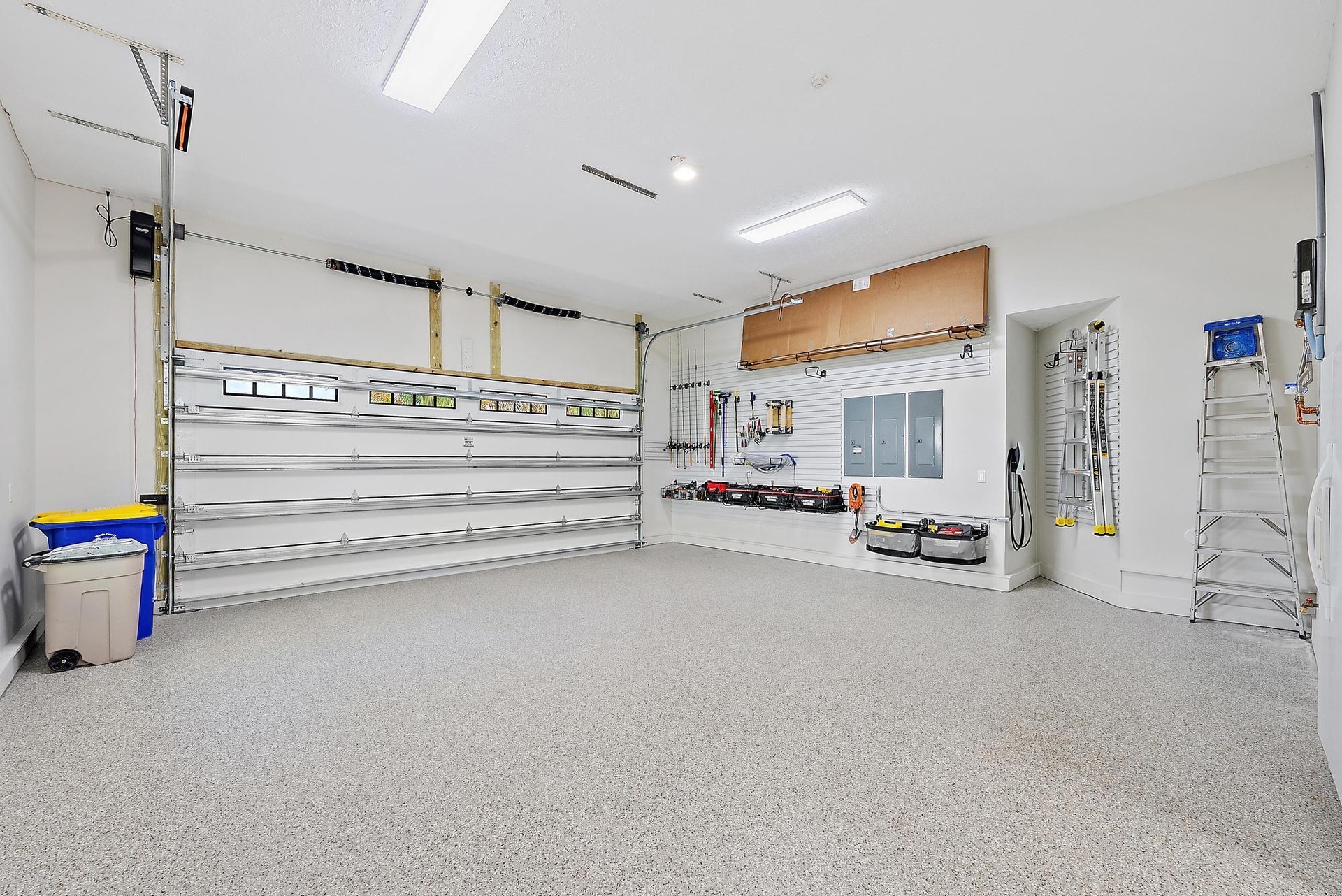 Spacious garage featuring an epoxy-coated floor, integrated wall-mounted slat board storage system, overhead fluorescent lighting, and a multi-panel s