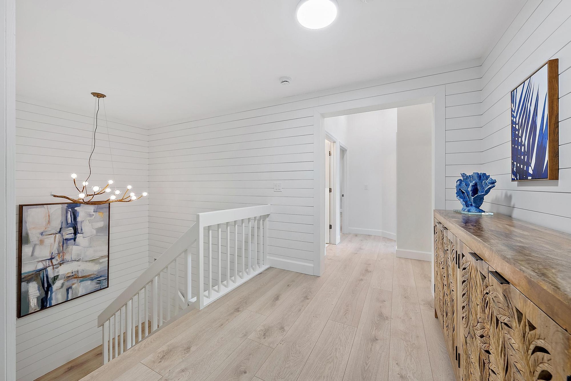 White shiplap wall paneling, wood-finish flooring, white staircase railing, and a multi-bulb branching chandelier