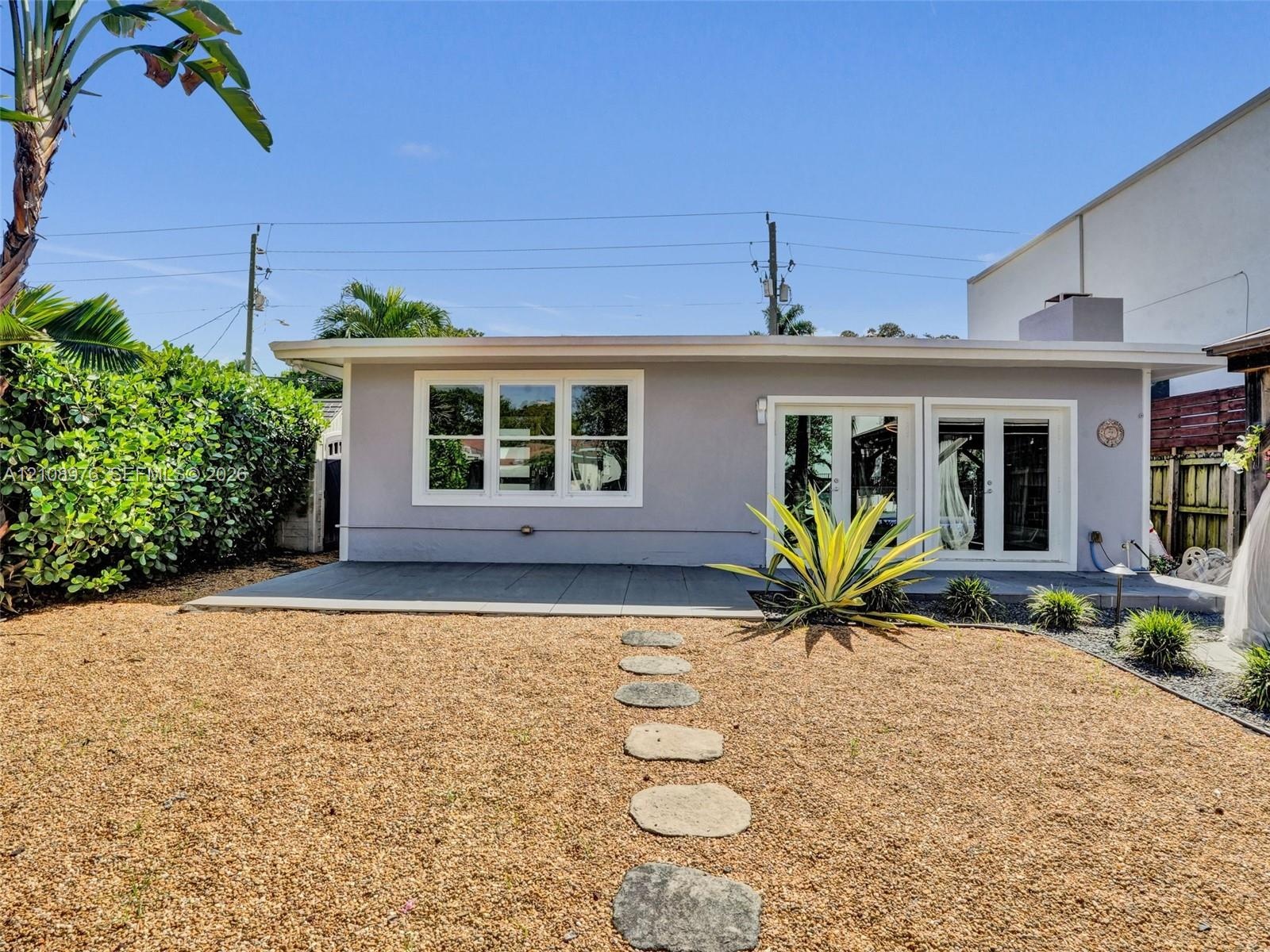 Rear exterior featuring a concrete patio, dual glass-paneled double doors, horizontal multi-pane windows, and a stone-paver walkway set within a grave