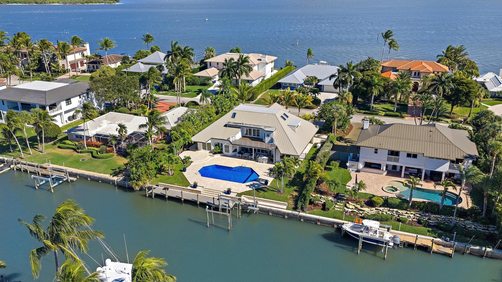 Waterfront property featuring a private boat dock, swimming pool, paved patio, and multi-level roofline