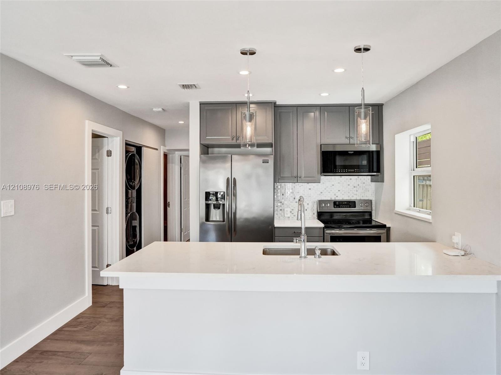 Kitchen featuring gray cabinetry, stainless steel appliances, white quartz countertops, mosaic tile backsplash, and dual pendant lighting
