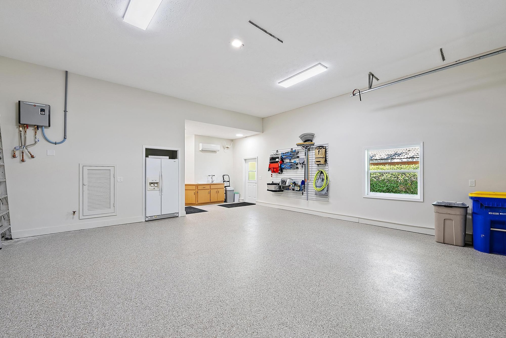 Garage interior featuring speckled epoxy flooring, built-in cabinetry, a wall-mounted ductless heating and cooling unit, overhead lighting, and a wind