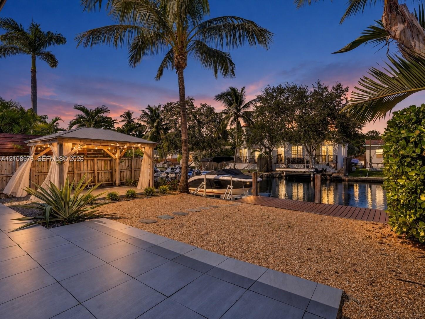 Waterfront property featuring a covered timber-framed gazebo, wooden dock, gravel landscaping, and large-format tile patio