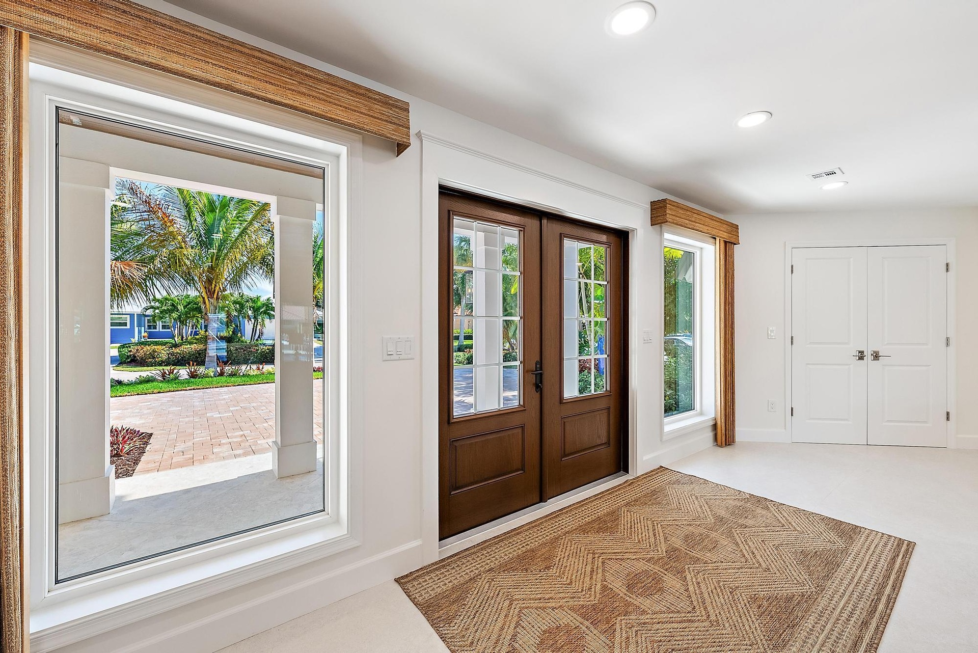 Double entry doors with divided-lite glass panels, neutral tile flooring, recessed ceiling lighting, and large picture windows featuring wood-finish v