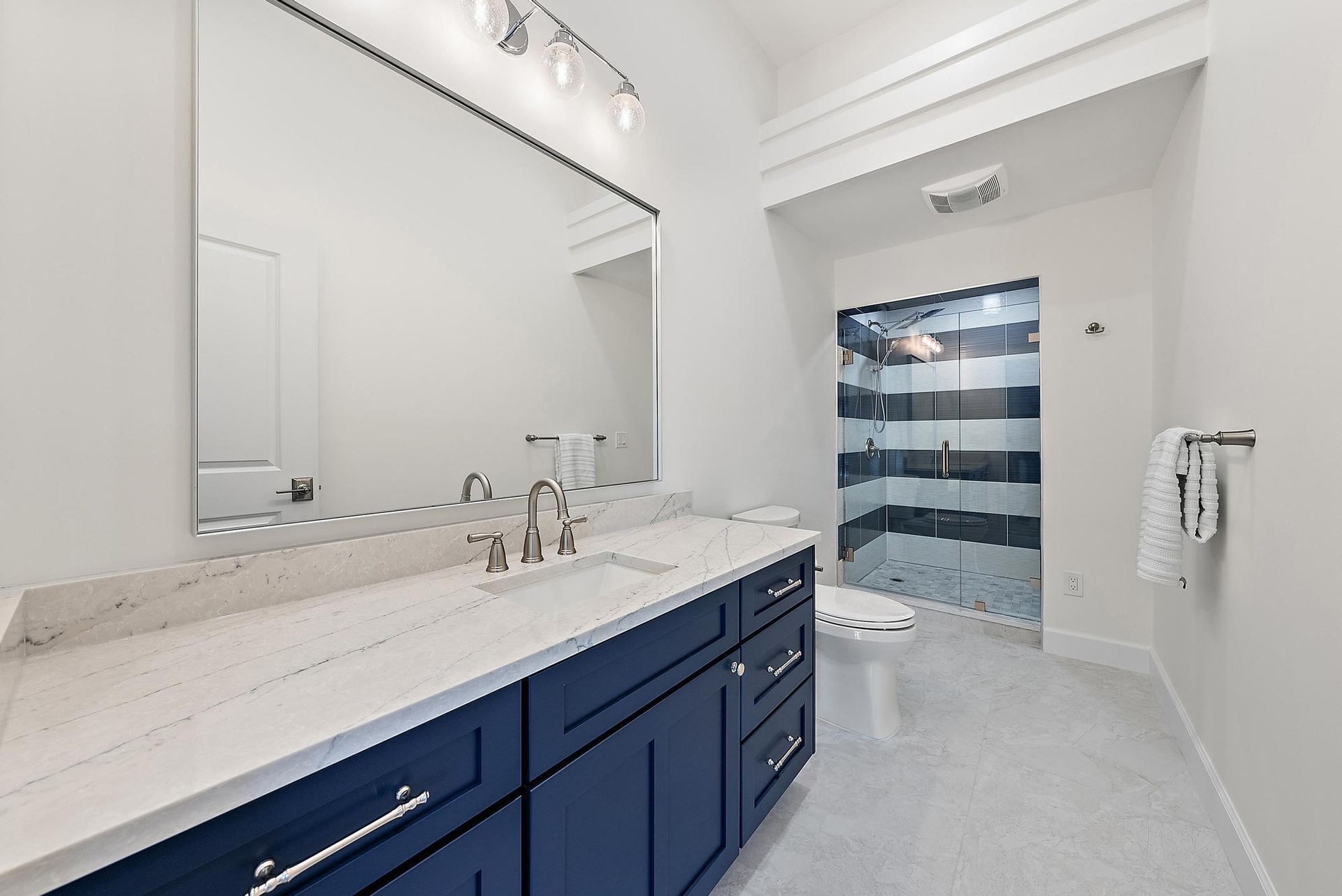Navy blue vanity with light-toned stone countertop, integrated sink, expansive wall-mounted mirror, and walk-in shower with horizontal tile pattern