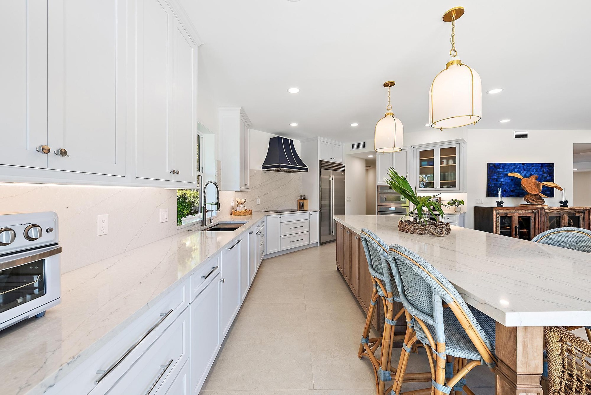 Kitchen featuring white shaker-style cabinetry, a large center island with stone-finish countertops, custom range hood, built-in stainless steel appli