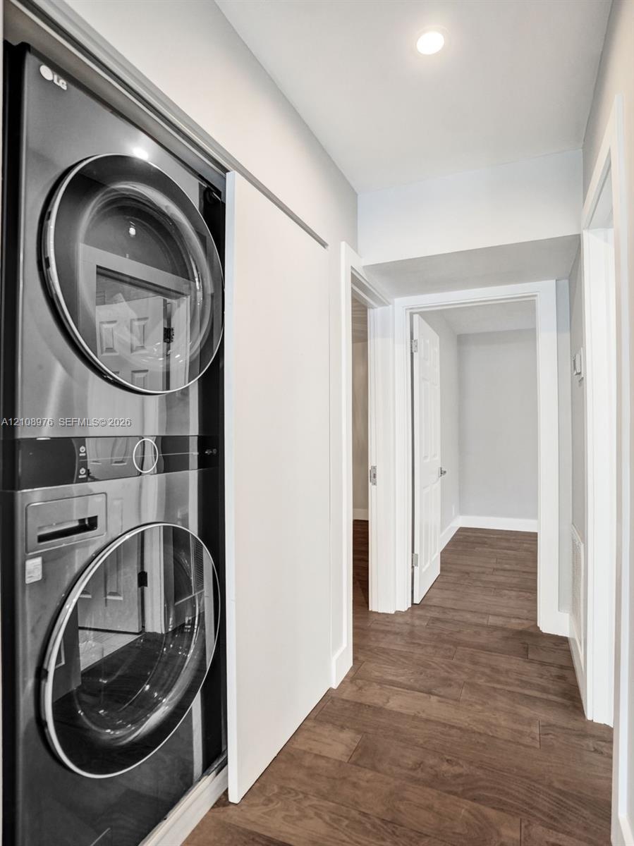 Laundry area featuring a stackable stainless steel appliance unit, recessed lighting, and wood-finish flooring
