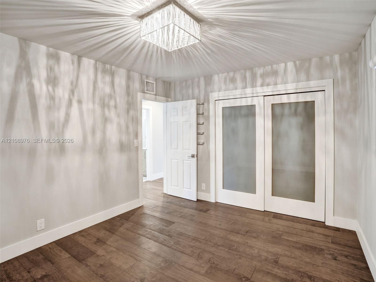 Wood-finish flooring featuring a square, multi-faceted crystal ceiling fixture, dual-panel sliding doors with frosted glass inserts, and a six-panel i