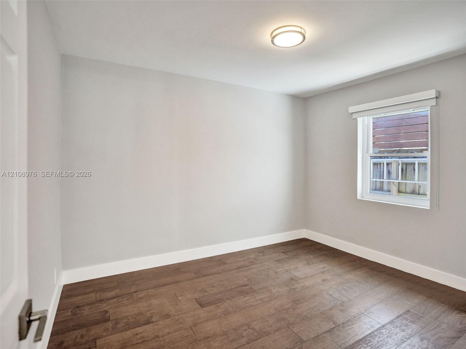 Bedroom 2. Interior space featuring neutral wall paint, wood-finish flooring, a flush-mount ceiling light fixture, and a single-hung window with a rol