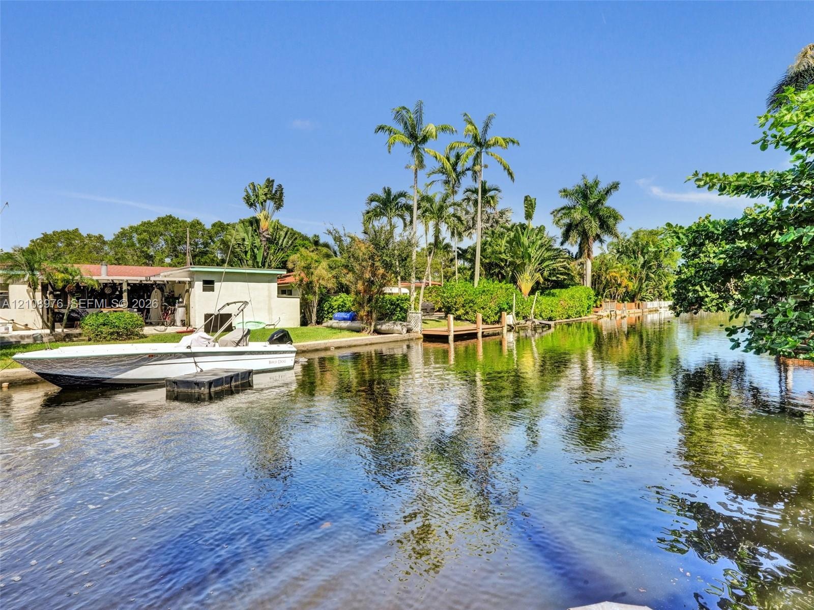 Waterfront property featuring a private wooden dock, bulkhead sea wall, and mature palm trees