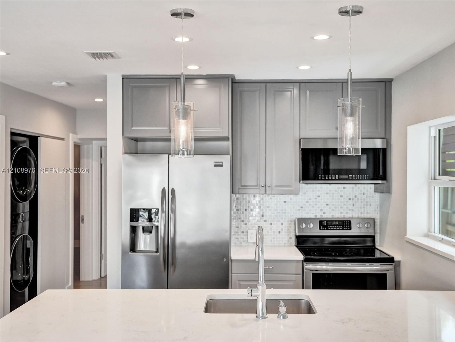 Kitchen featuring grey shaker-style cabinetry, stainless steel appliances, white stone-finish countertops, a mosaic tile backsplash, and dual glass pe