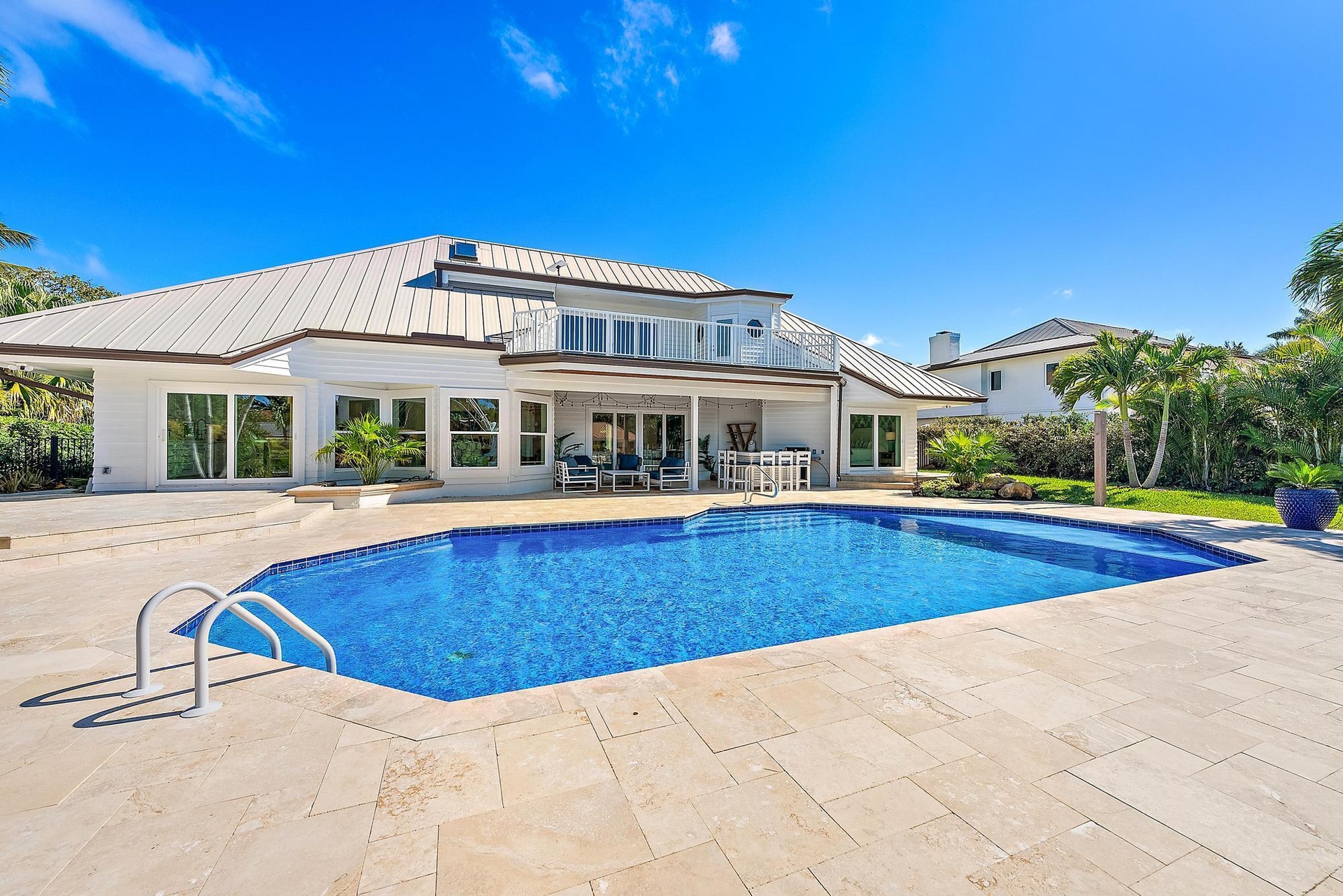 Exterior featuring a metal roof, second-story balcony with railings, stone-paver pool deck, and an in-ground swimming pool