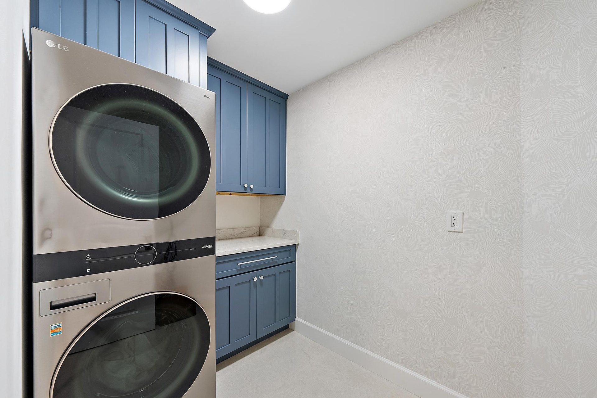 Laundry area featuring custom blue shaker-style cabinetry, stone-surface countertop, and stainless steel stacked appliance unit