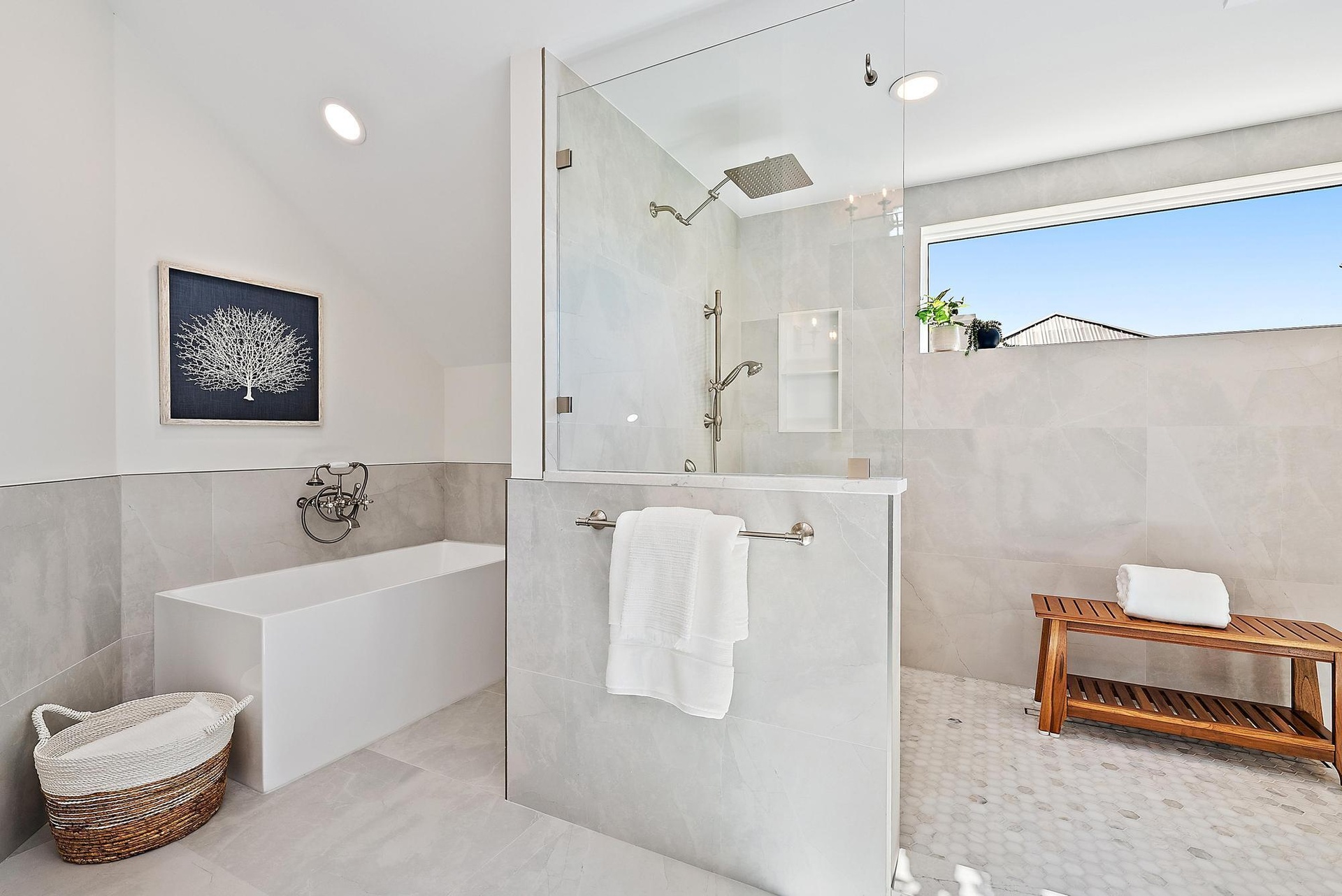 Freestanding rectangular soaking tub with wall-mounted faucet, walk-in shower with frameless glass enclosure, rainfall showerhead, and neutral large-f