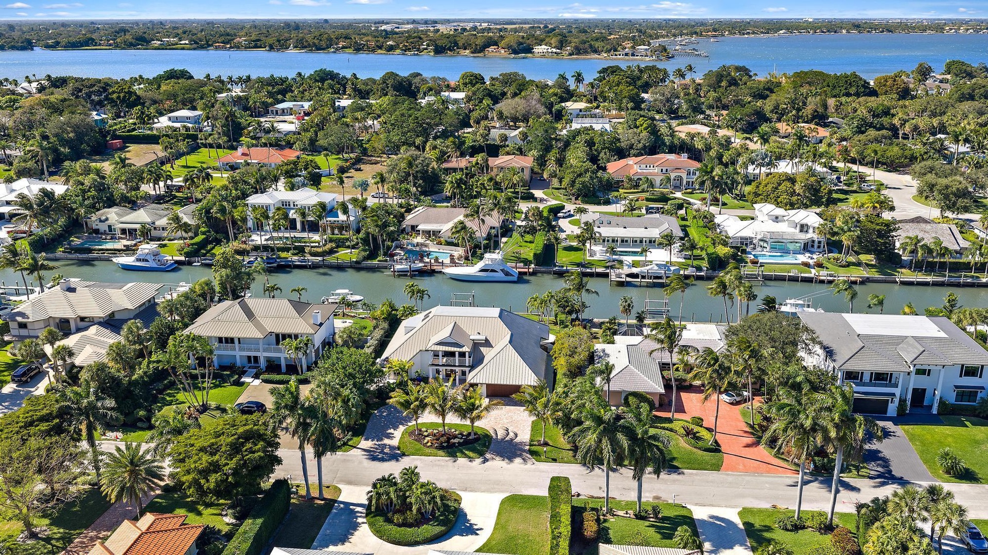Aerial perspective of a waterfront community featuring deep-water canal access, private boat docks, paved driveways, manicured tropical landscaping, a