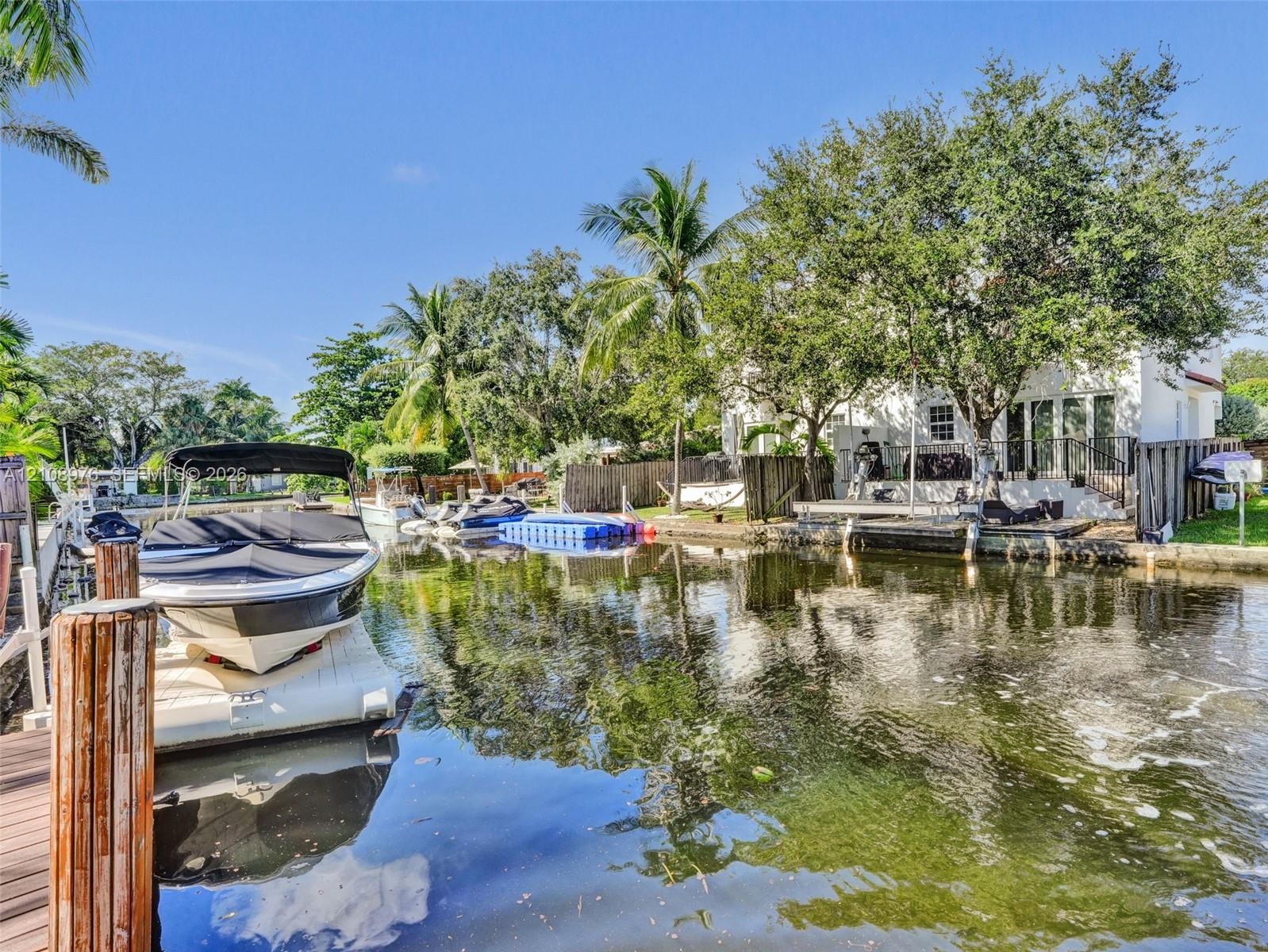 Waterfront property featuring a private boat lift, concrete bulkhead, mature trees, and direct canal access