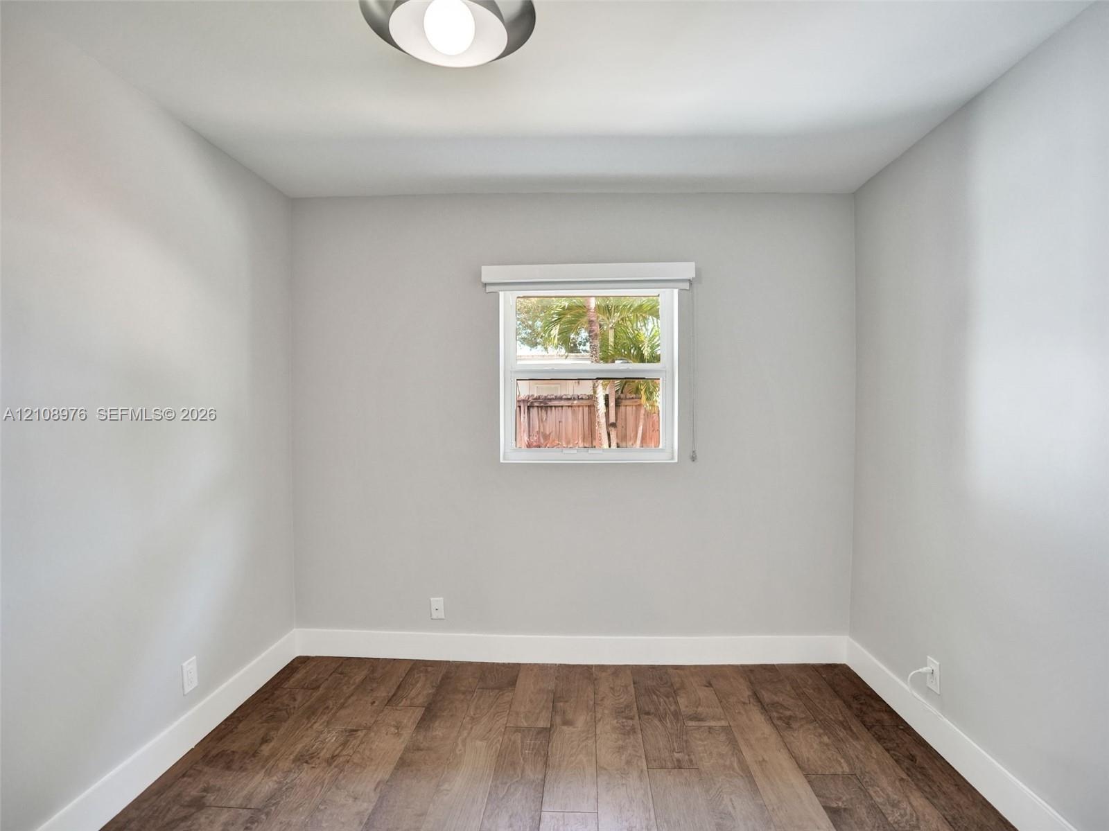 Bedroom 3. Neutral wall paint, wood-finish flooring, and single-pane window with installed window treatment, complemented by a flush-mount ceiling fix