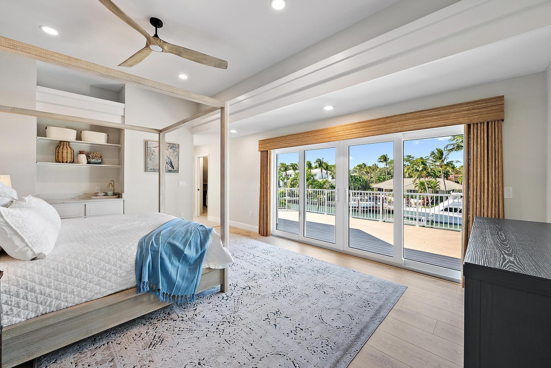 Recessed lighting, wood-finish flooring, built-in recessed shelving, ceiling fan with wood-finish blades, and expansive sliding glass doors opening to