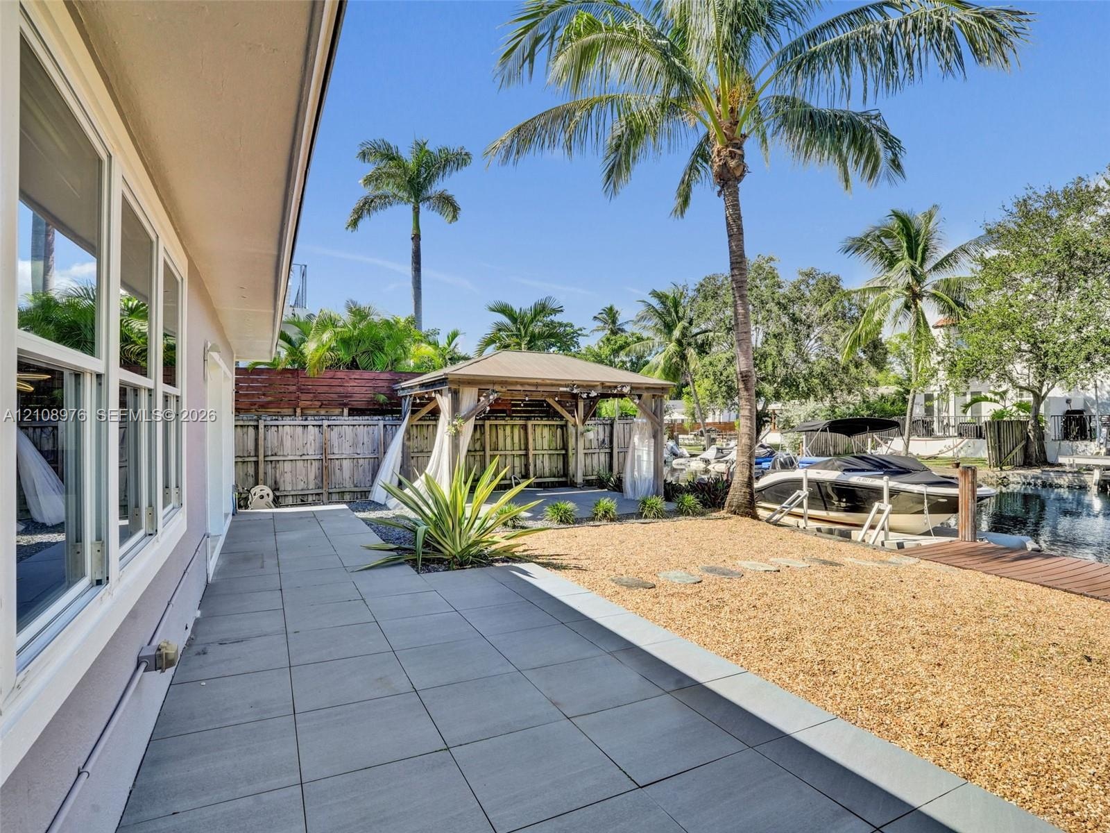 Rear outdoor area featuring a stone-tile patio, a gravel landscape, a wooden pergola, and a private dock